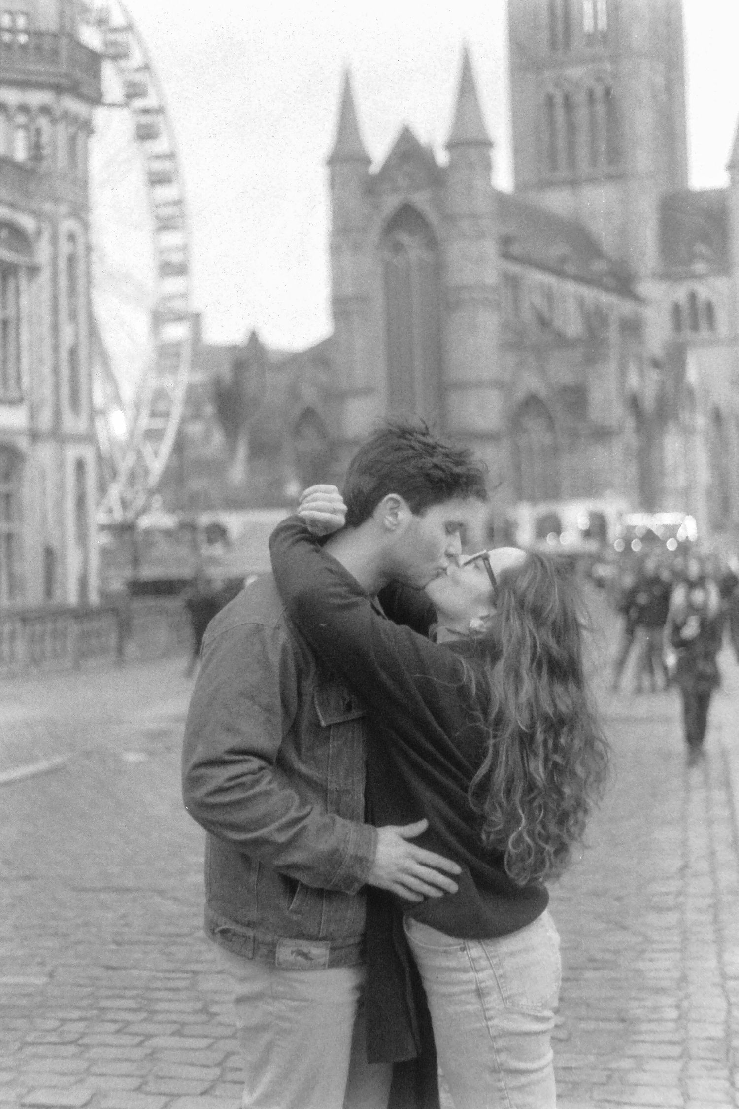 Couple sharing a romantic kiss in a European city square in black and white.