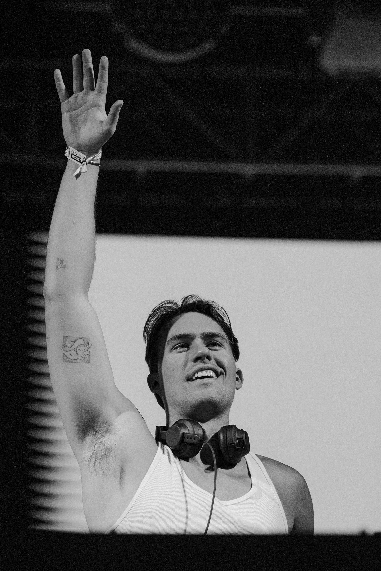 Black and white photo of smiling DJ with headphones raising hand at outdoor music festival.