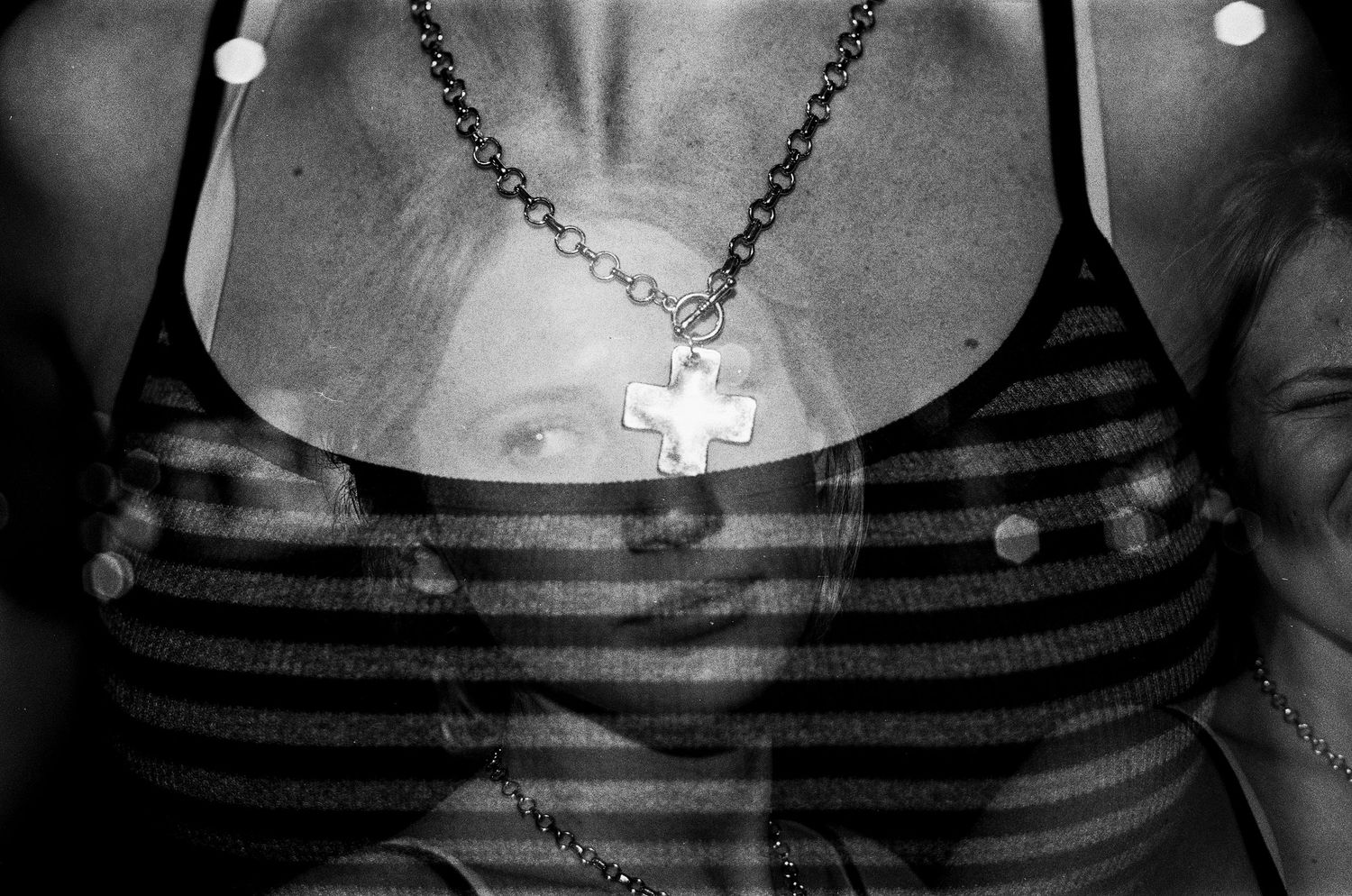 Black and white photo of woman wearing striped top and silver cross necklace with double exposure effect.