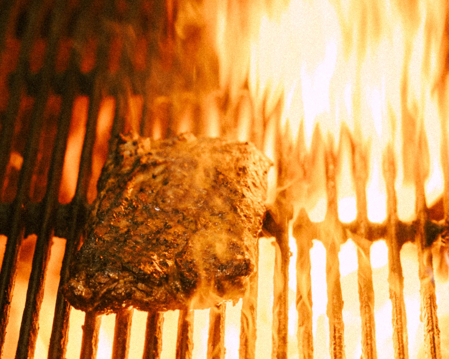 Steak searing on a flaming hot grill with bright orange fire flames.