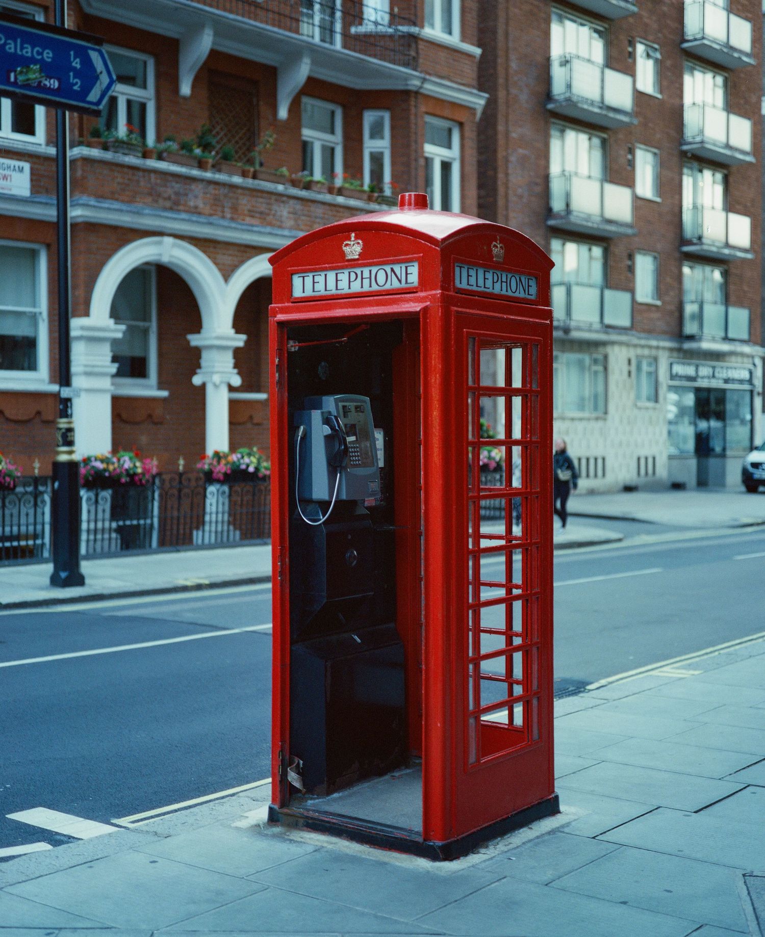 A classic red British telephone box on a London street corner, with a brick building in the background.