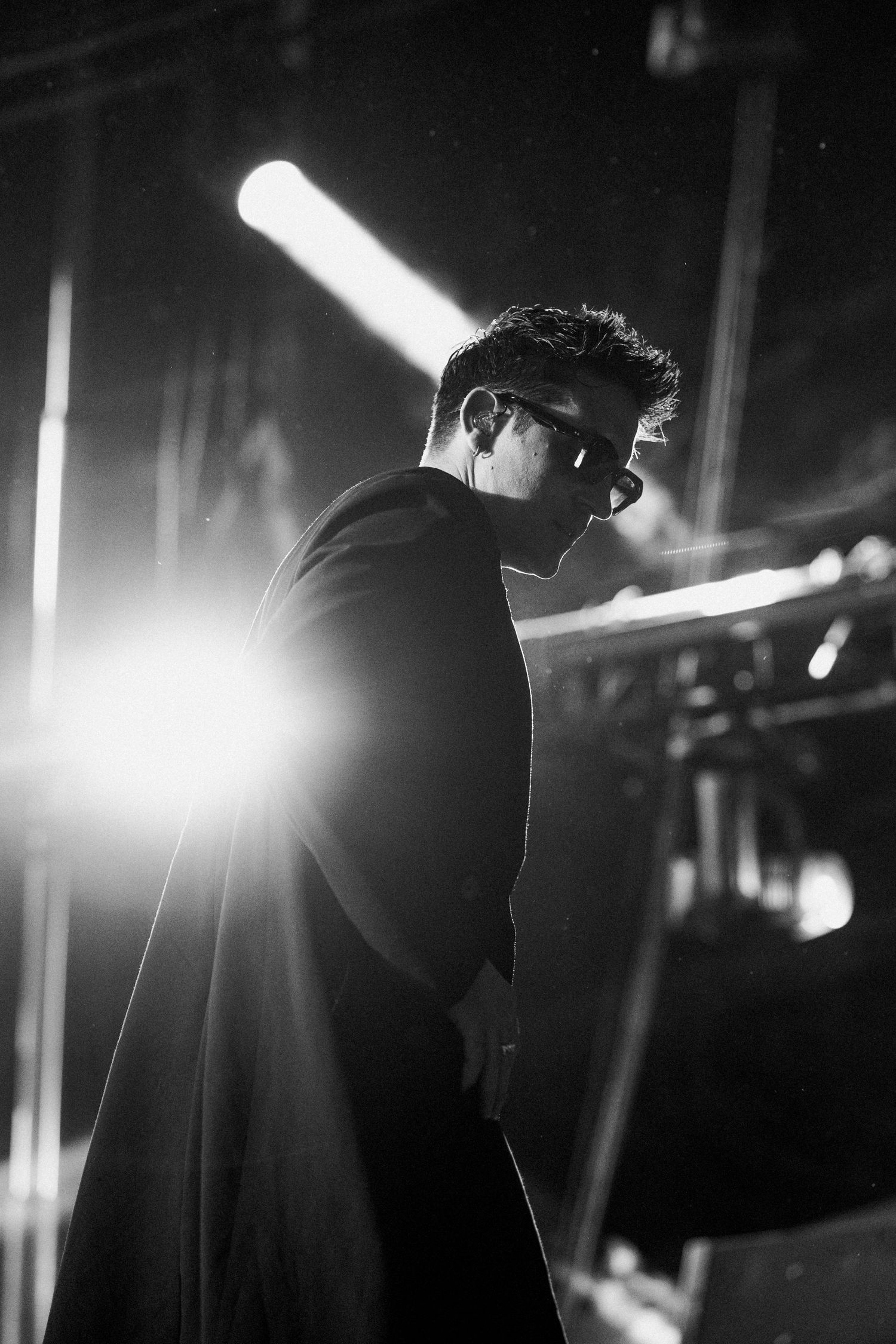 Black and white photo of a male performer on stage with dramatic backlight and stage lighting.