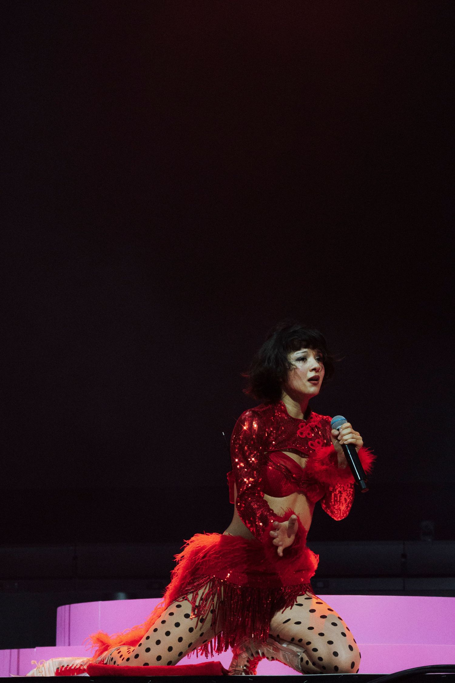 Female performer in red sequined outfit with fringe skirt and polka dot tights singing on stage.