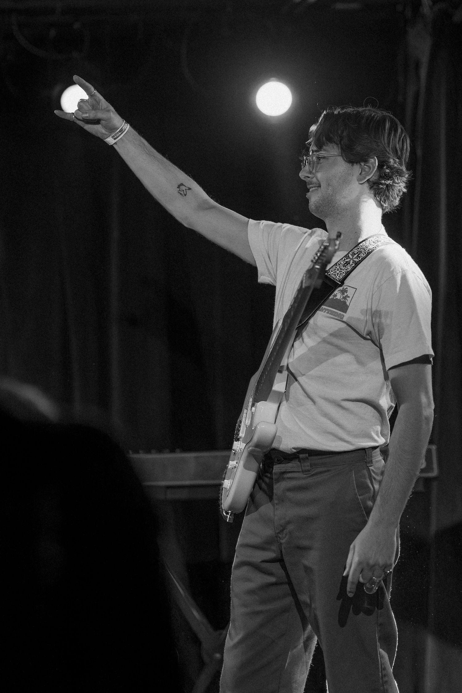 Male guitarist raises light to crowd in black and white live performance photo.