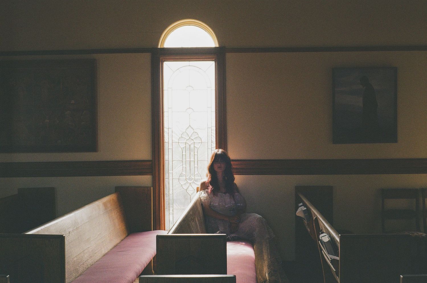 Woman sitting alone in church pew gazing at sunlit stained glass window in quiet contemplation. Artist: Victoria Bigelow