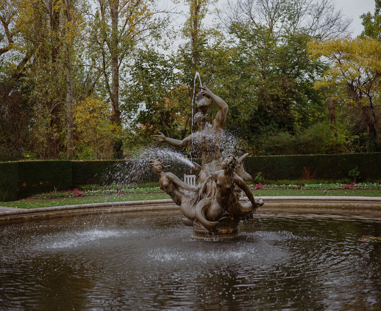 Bronze mythological fountain sculpture with water jets in an autumn garden park setting.