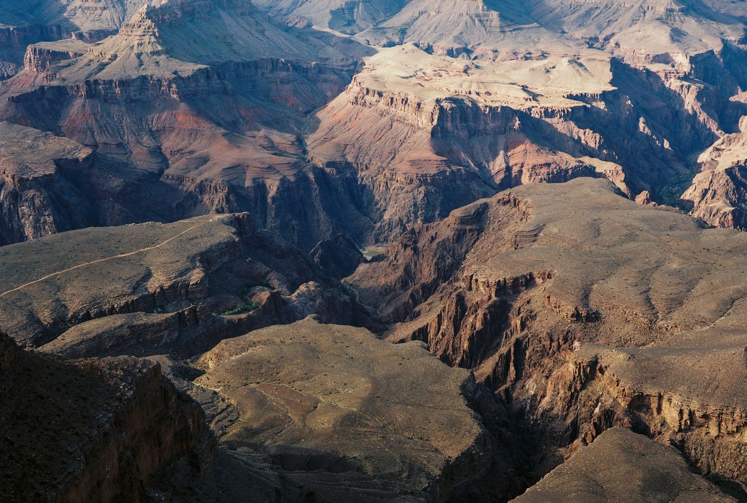 Aerial view of the Grand Canyon showcasing layered red rock formations and deep shadowed gorges in warm sunlight.