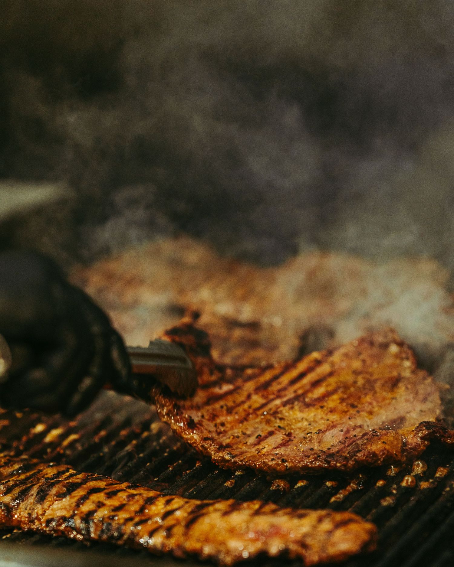 Juicy seasoned steak grilling on a hot barbecue grill with smoke rising.