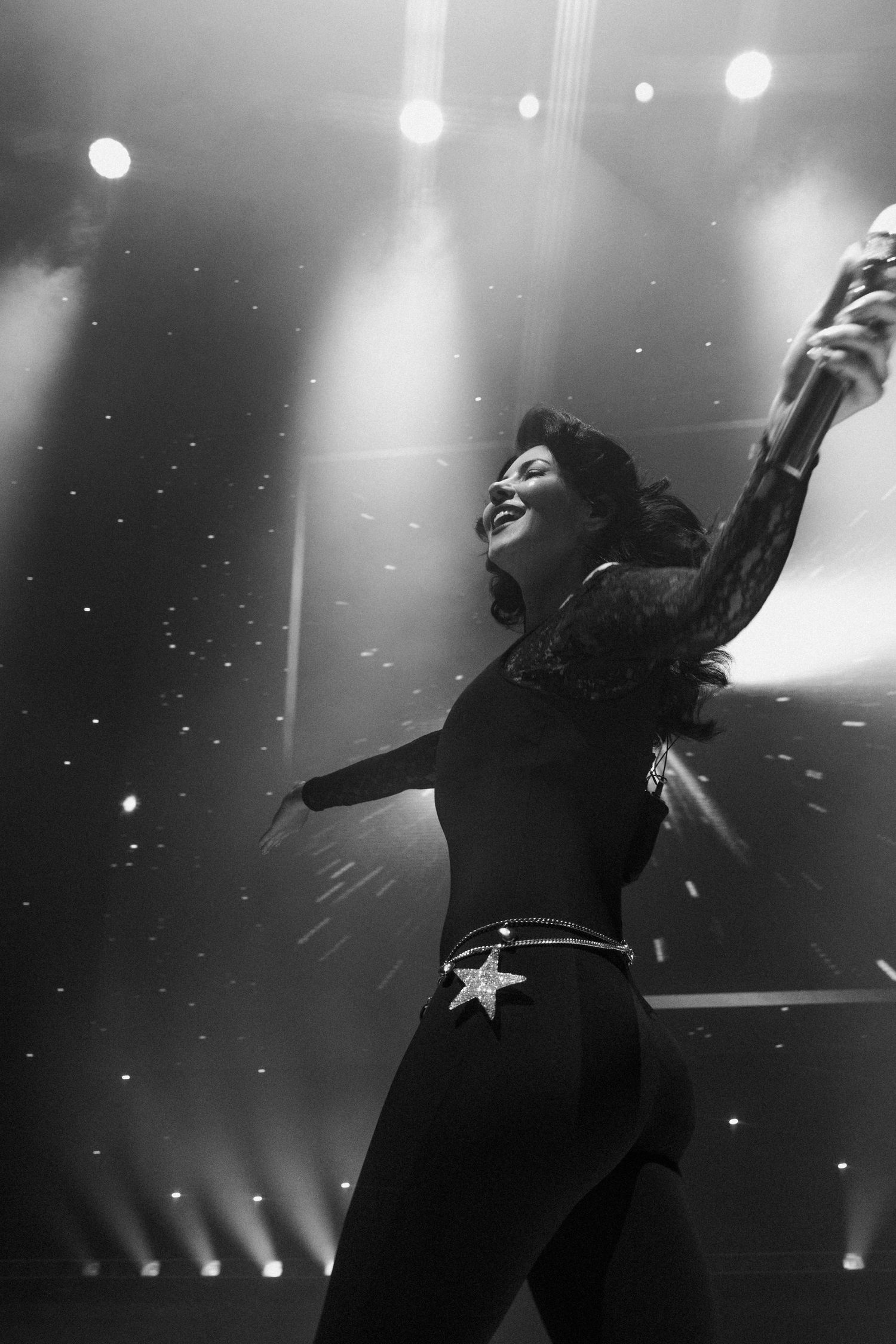 Black and white photo of a woman dancing on stage under bright spotlights, wearing a star belt buckle.