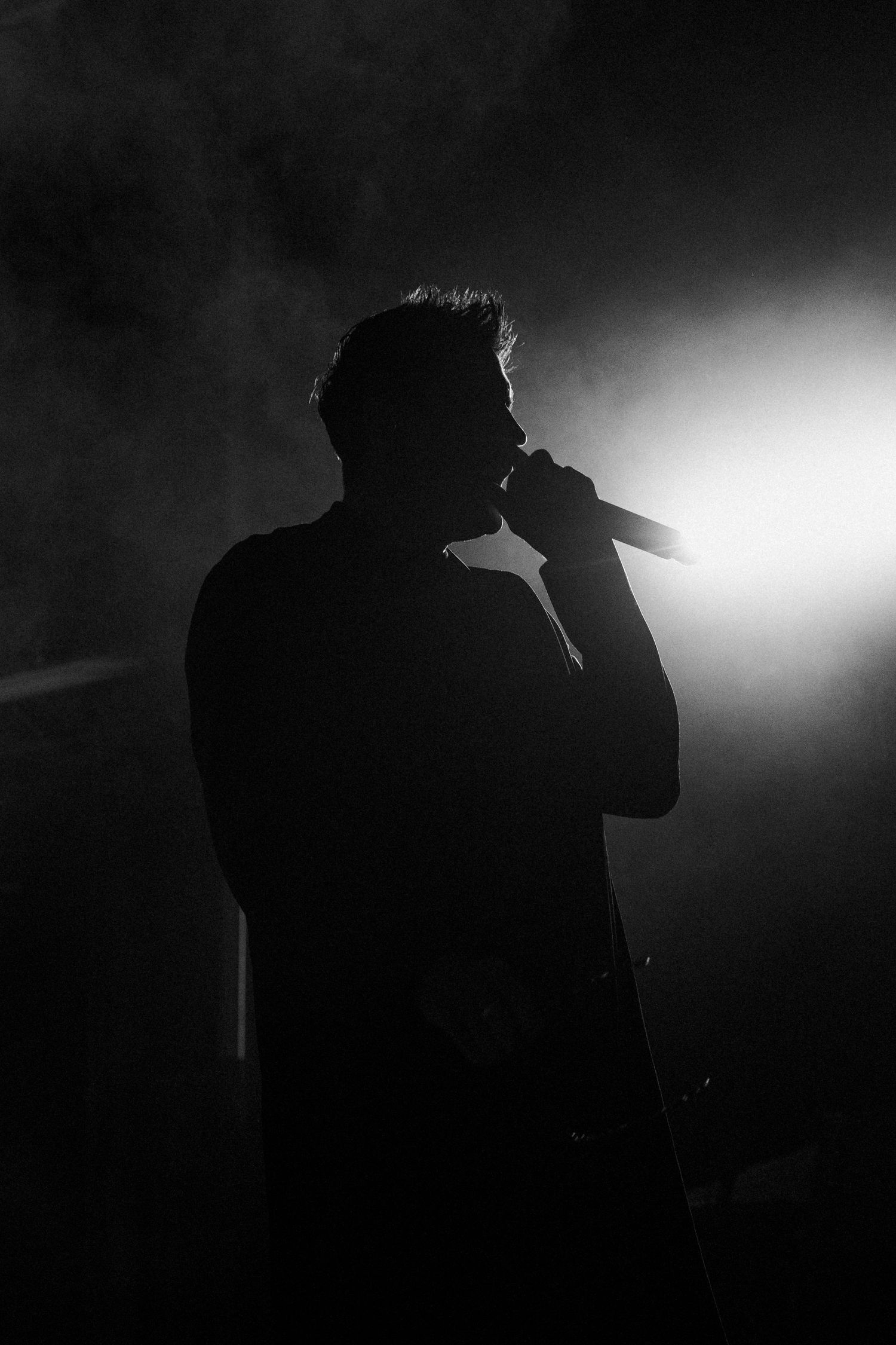 Dramatic black and white silhouette of a male singer performing with microphone in smoky stage lighting.