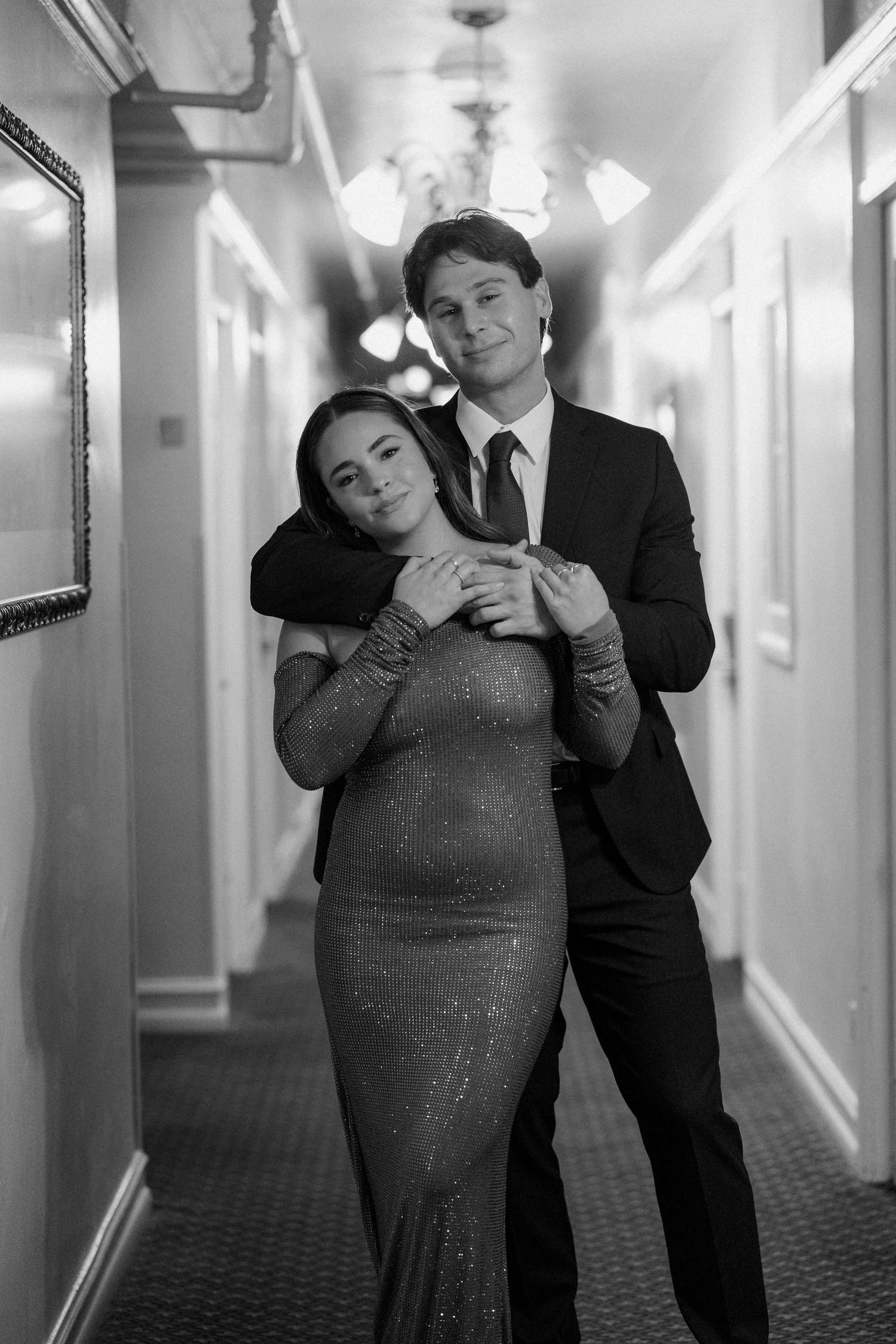 Couple posing elegantly in a hotel hallway, woman in sequin gown, man in suit.