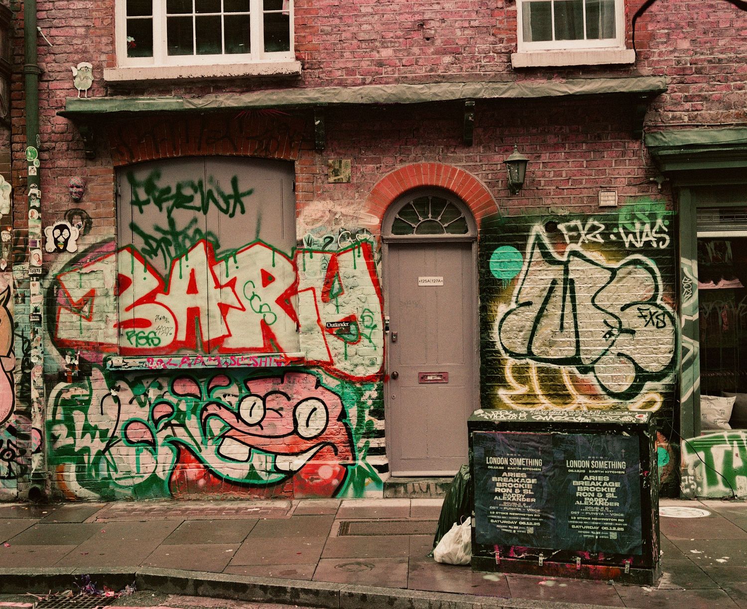 Colorful graffiti street art covers the brick walls and boarded windows of an urban building facade.