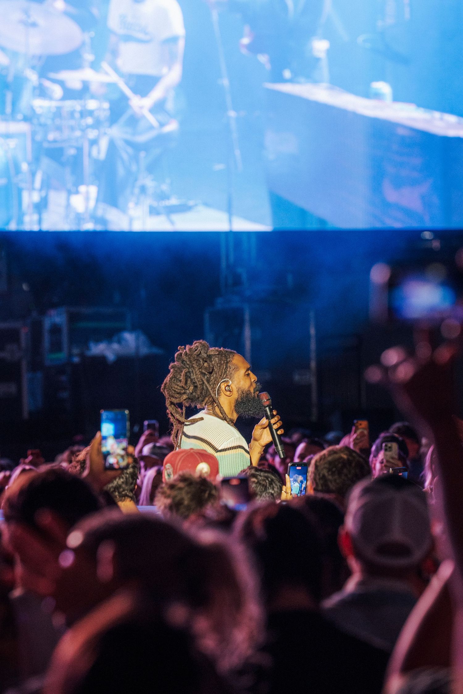 Crowd at a live concert with a large illustrated portrait of a performer displayed above the audience. Thee Sacred Souls 2025