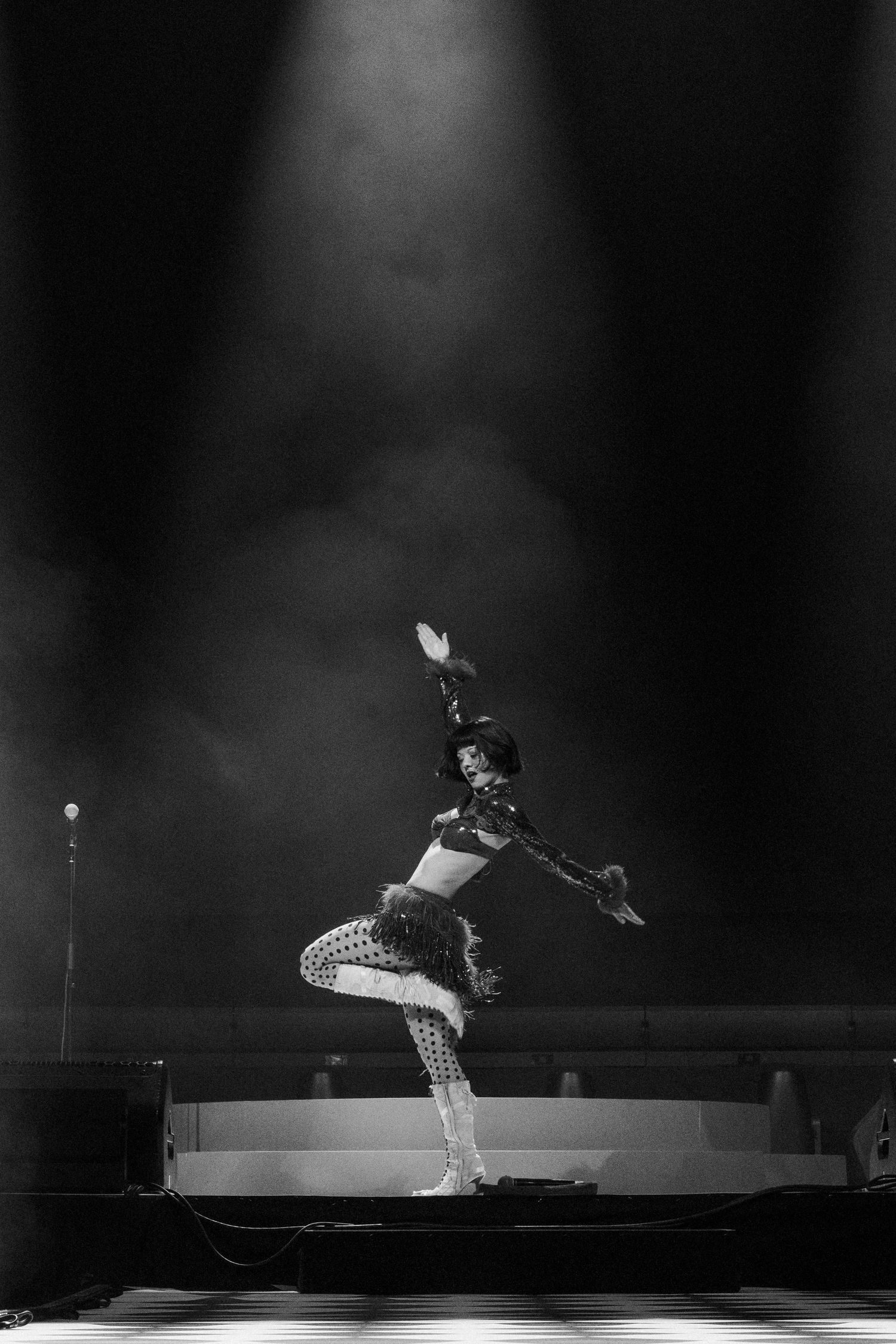 Black and white photo of a dancer performing on stage under a spotlight in a ruffled costume.