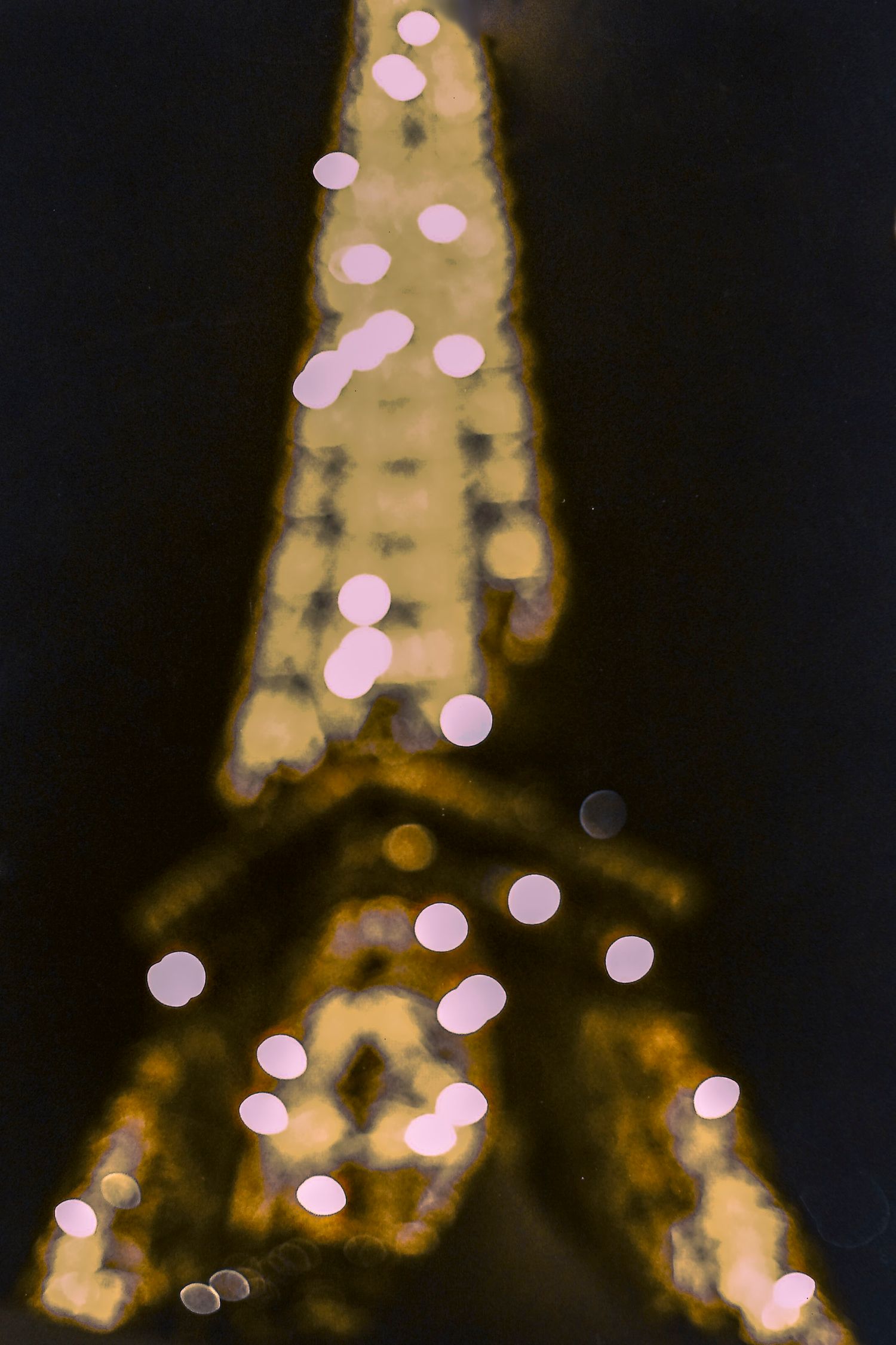 Blurry bokeh photo of the illuminated Eiffel Tower at night with sparkling pink and gold lights in Paris.