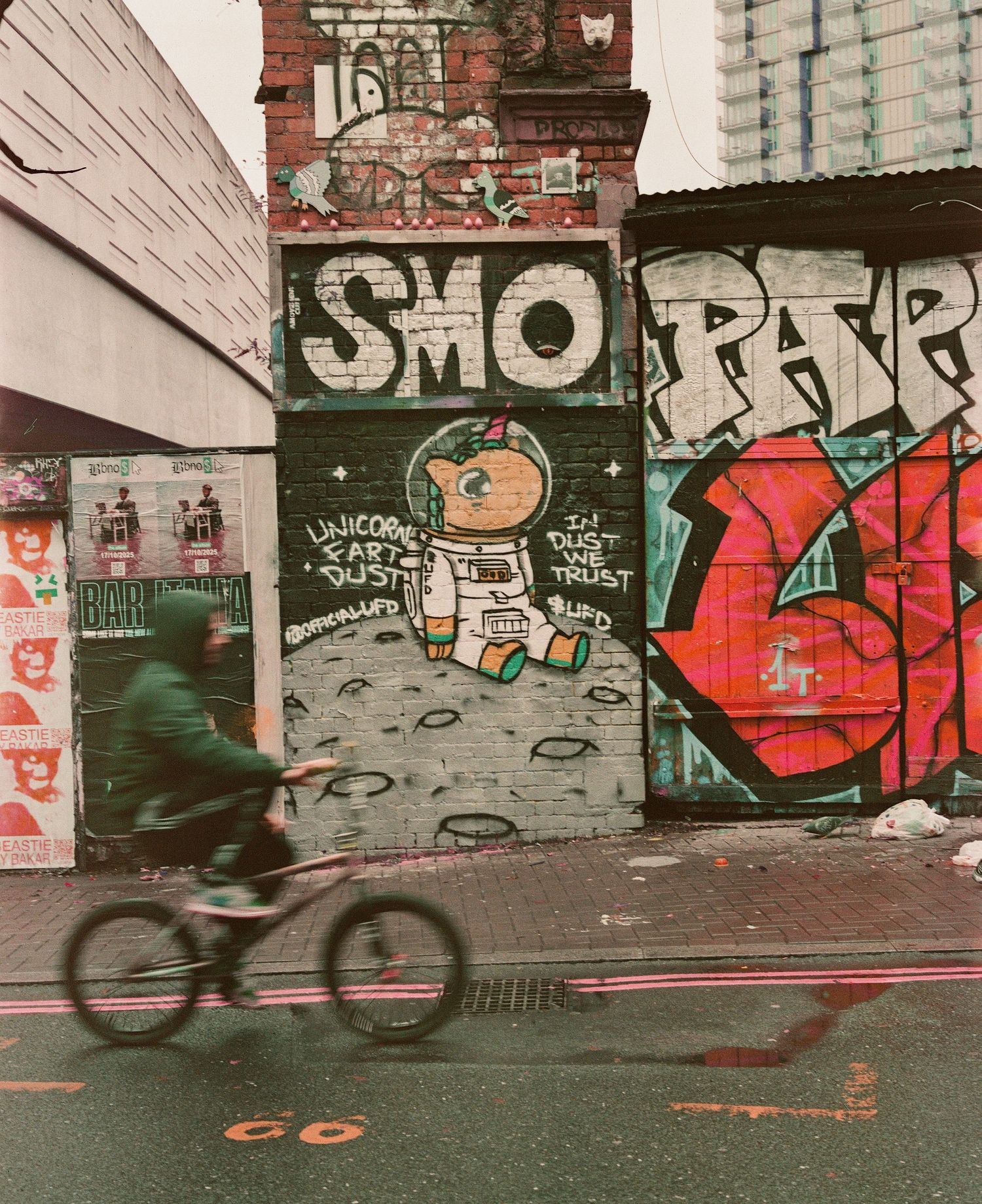 Cyclist rides past colorful graffiti murals on urban brick walls in city street.