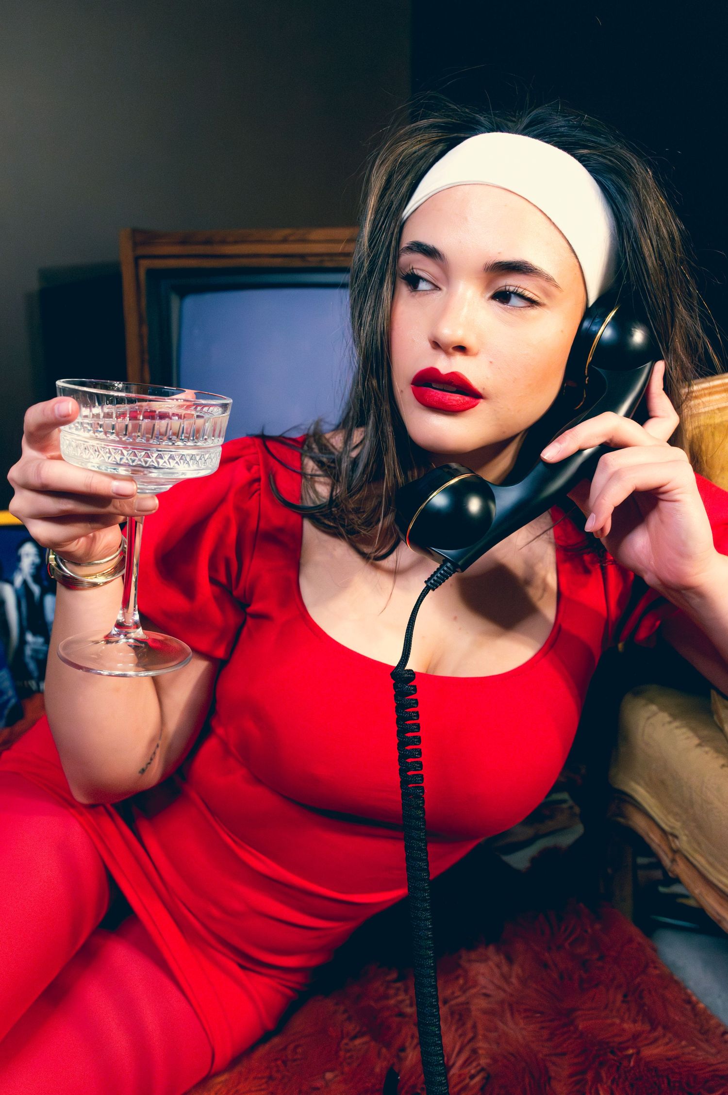 Woman in red dress with red lips holding a cocktail glass and vintage telephone receiver.