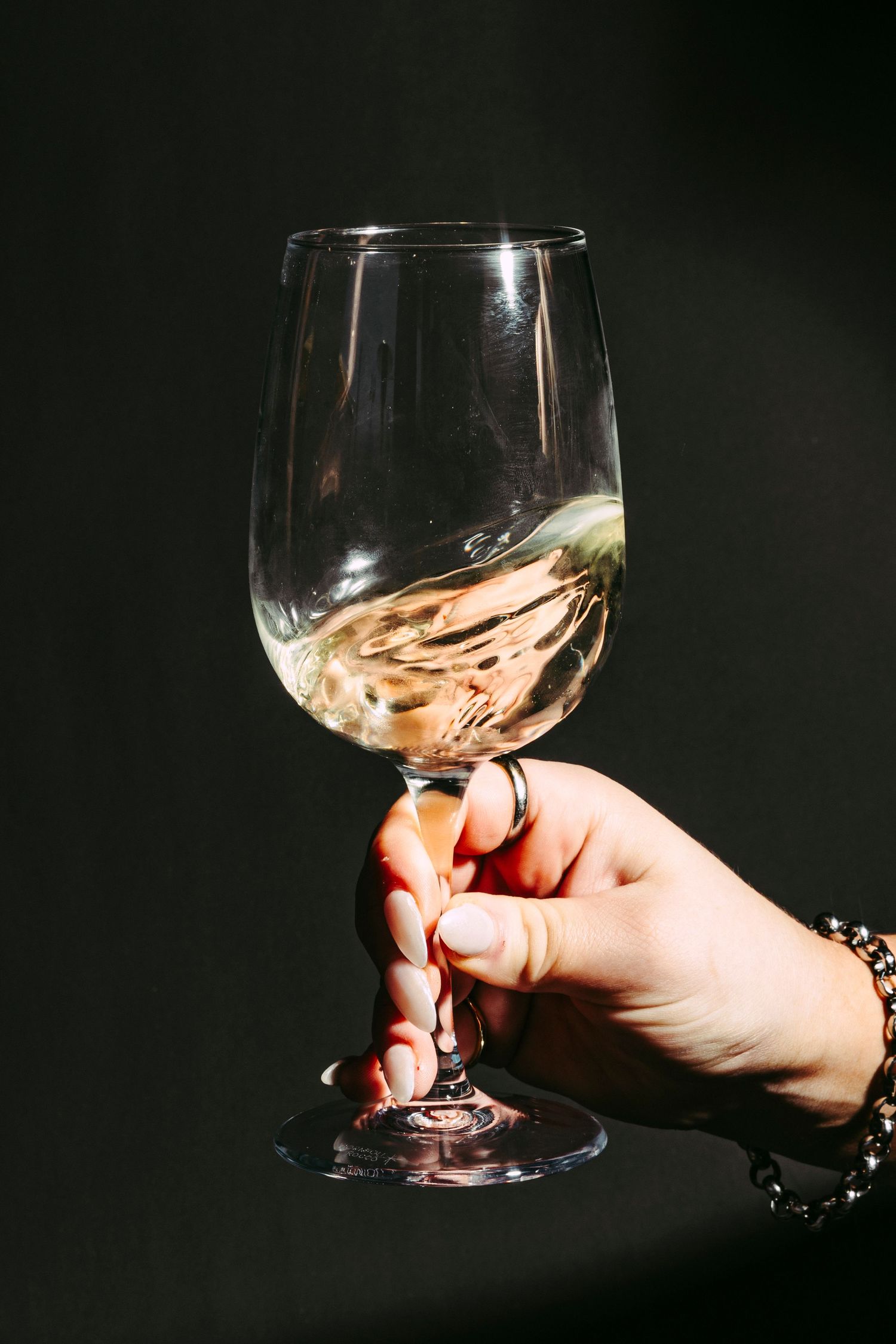 Hand holding a wine glass with swirling white wine against a dark background.