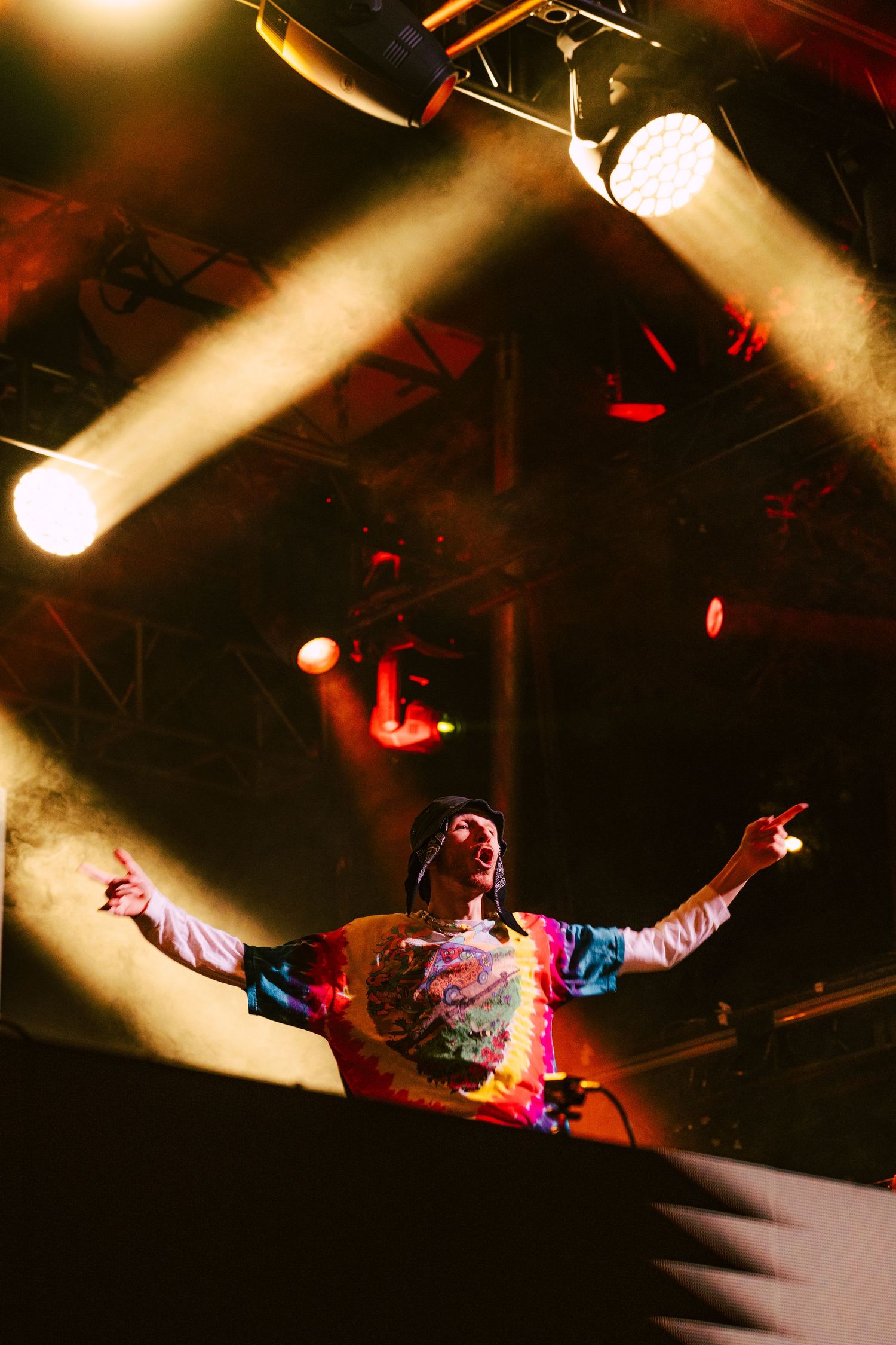 Performer in colorful shirt with arms outstretched on stage bathed in warm golden stage lights.