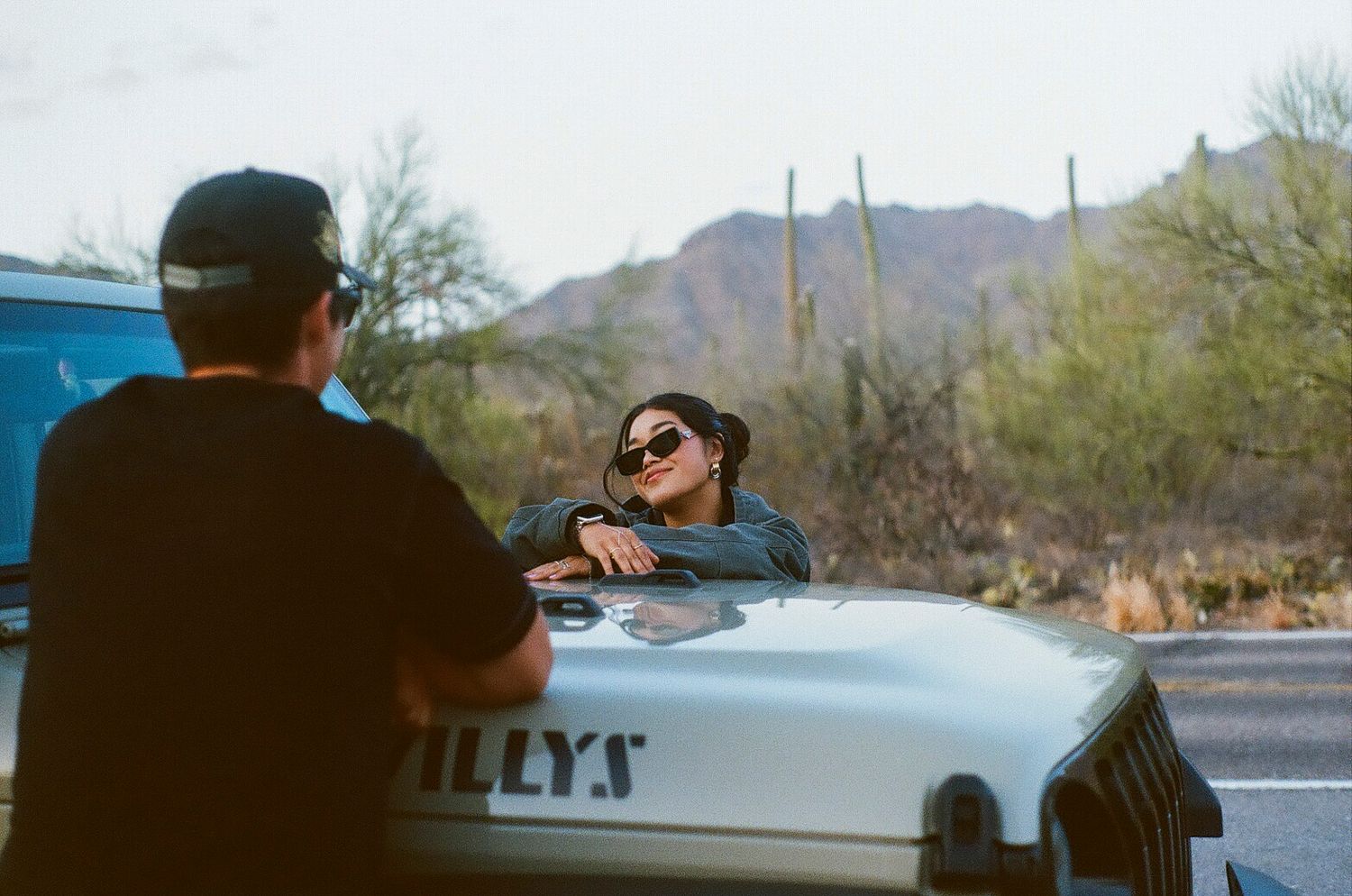Woman leaning on a vintage Willys vehicle talking to a man in desert setting.