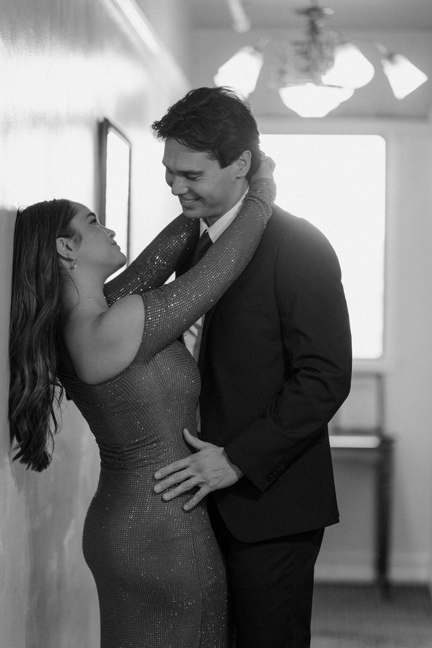 Elegant couple in formal wear sharing an intimate moment in black and white photo.