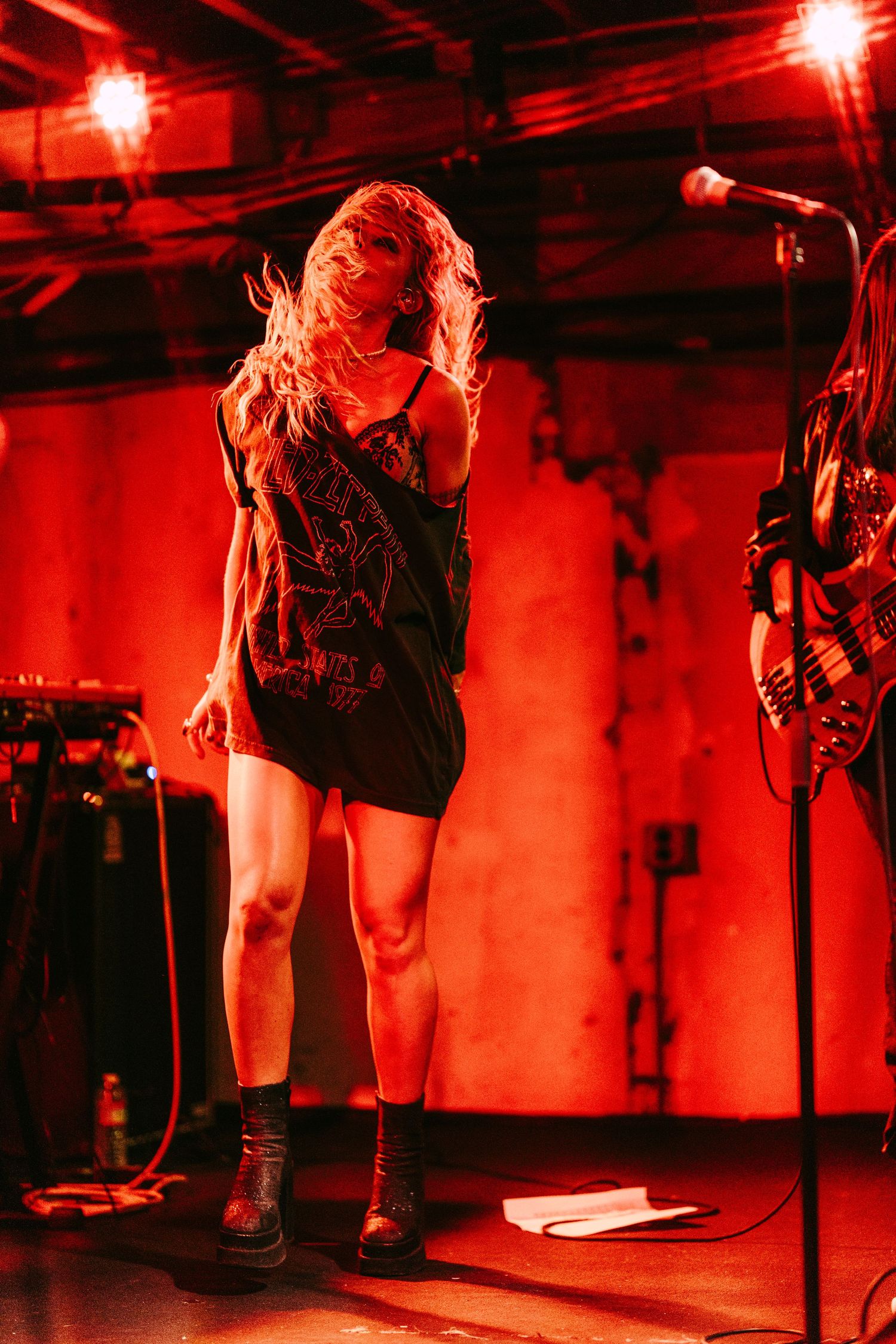 Female performer on stage under red lights in a dark graphic tee and boots.