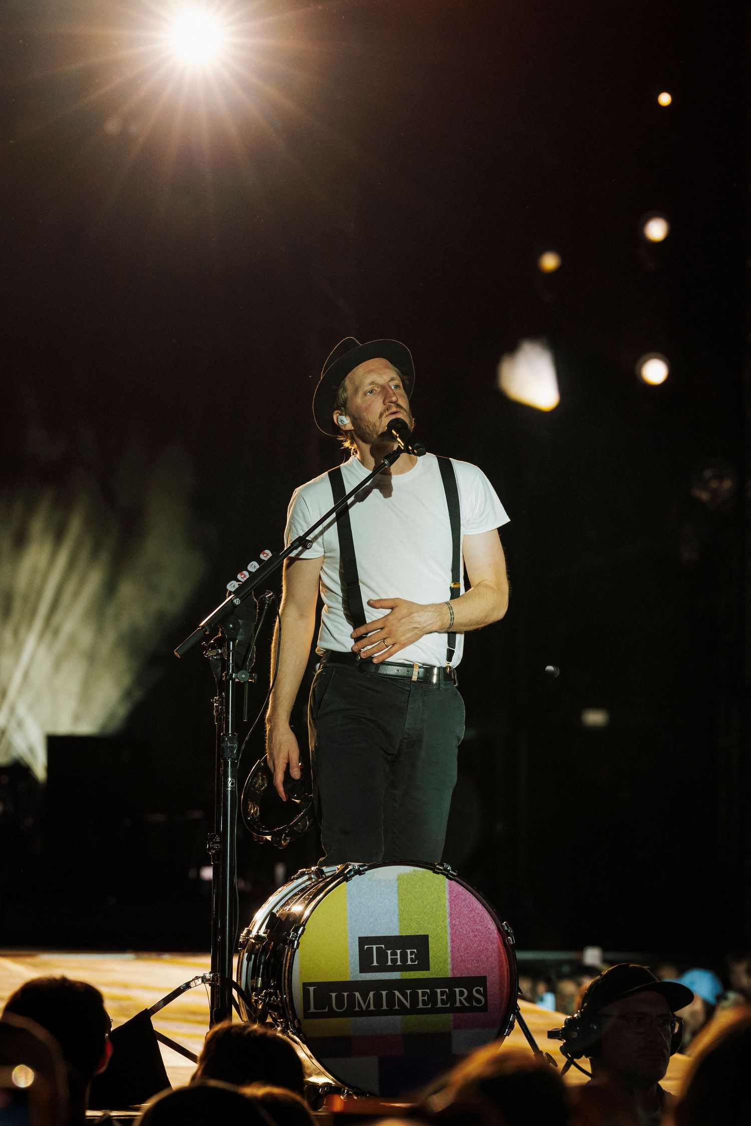 The Lumineers performer on stage in white shirt and suspenders with band logo visible on bass drum.