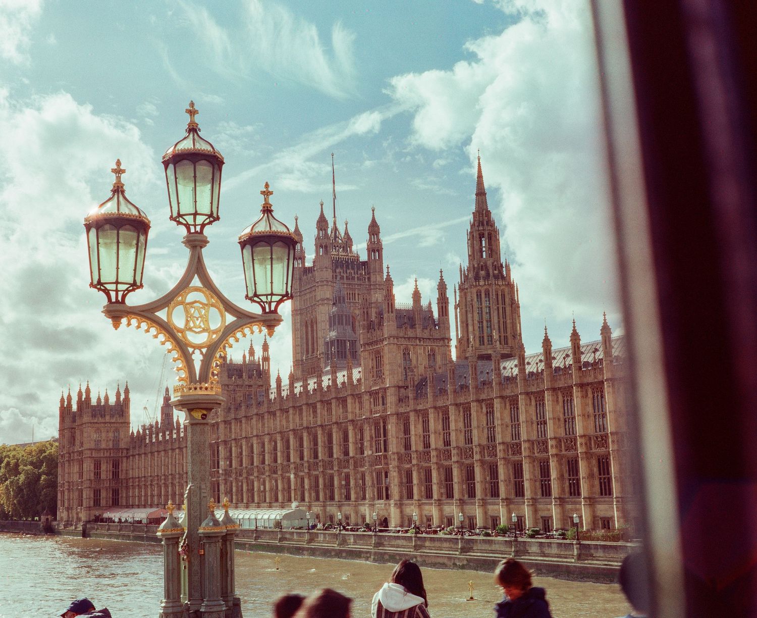 Ornate Victorian lamp post frames the iconic Houses of Parliament along the River Thames in London.