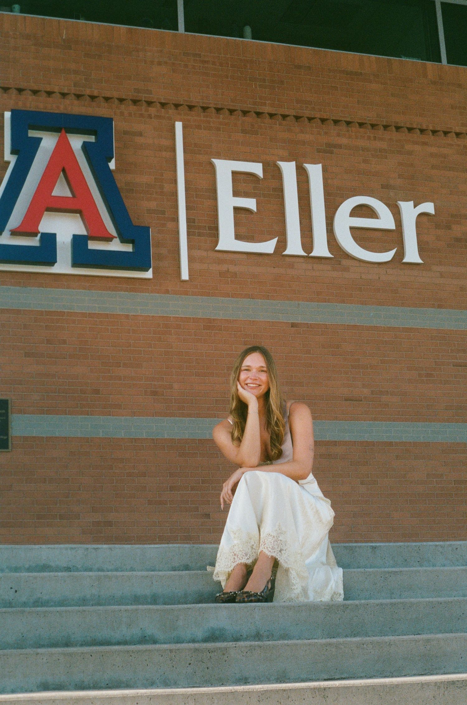 Smiling woman sitting on steps below University of Arizona Eller College sign.