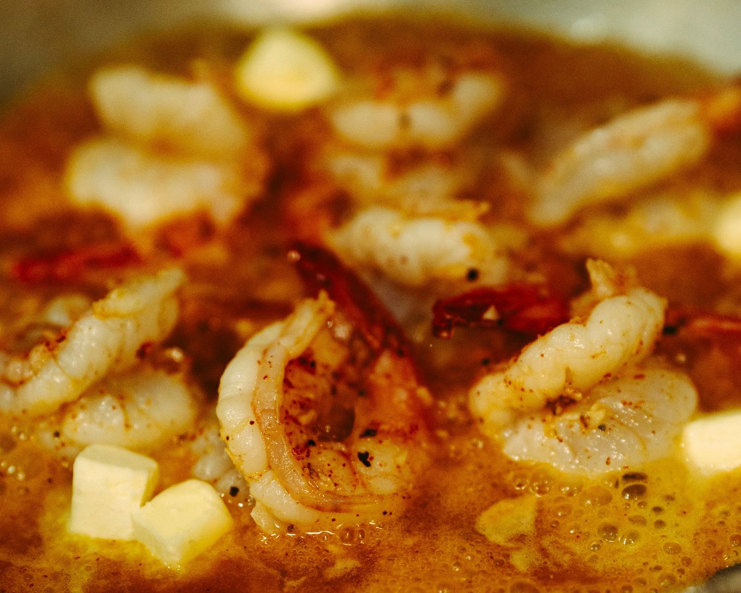 Shrimp sautéing in a rich buttery sauce with spices and garlic in a pan.