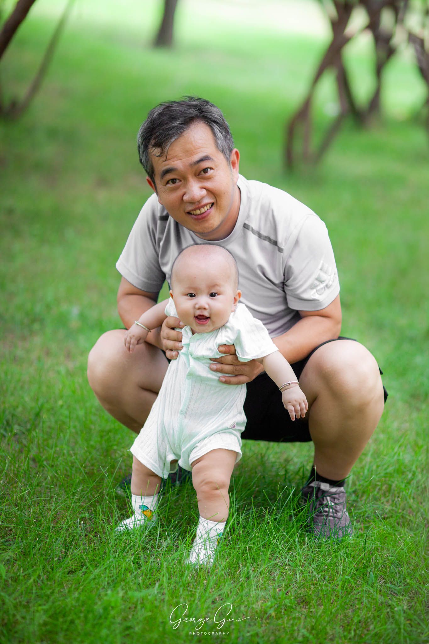 Father playing with his infant child on a green lawn in summer, captured by George Guo Photographer