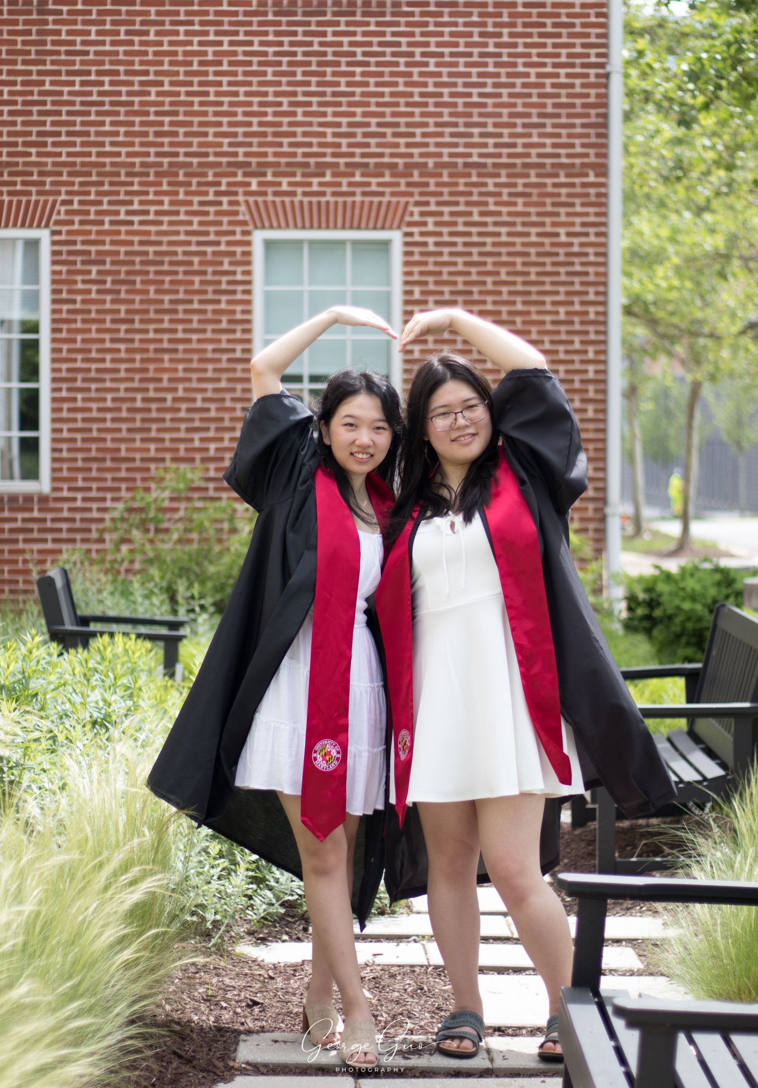 Two student girls making a heart shape with their hands to celebrate graduation on a college campus, captured by George Guo Photographer