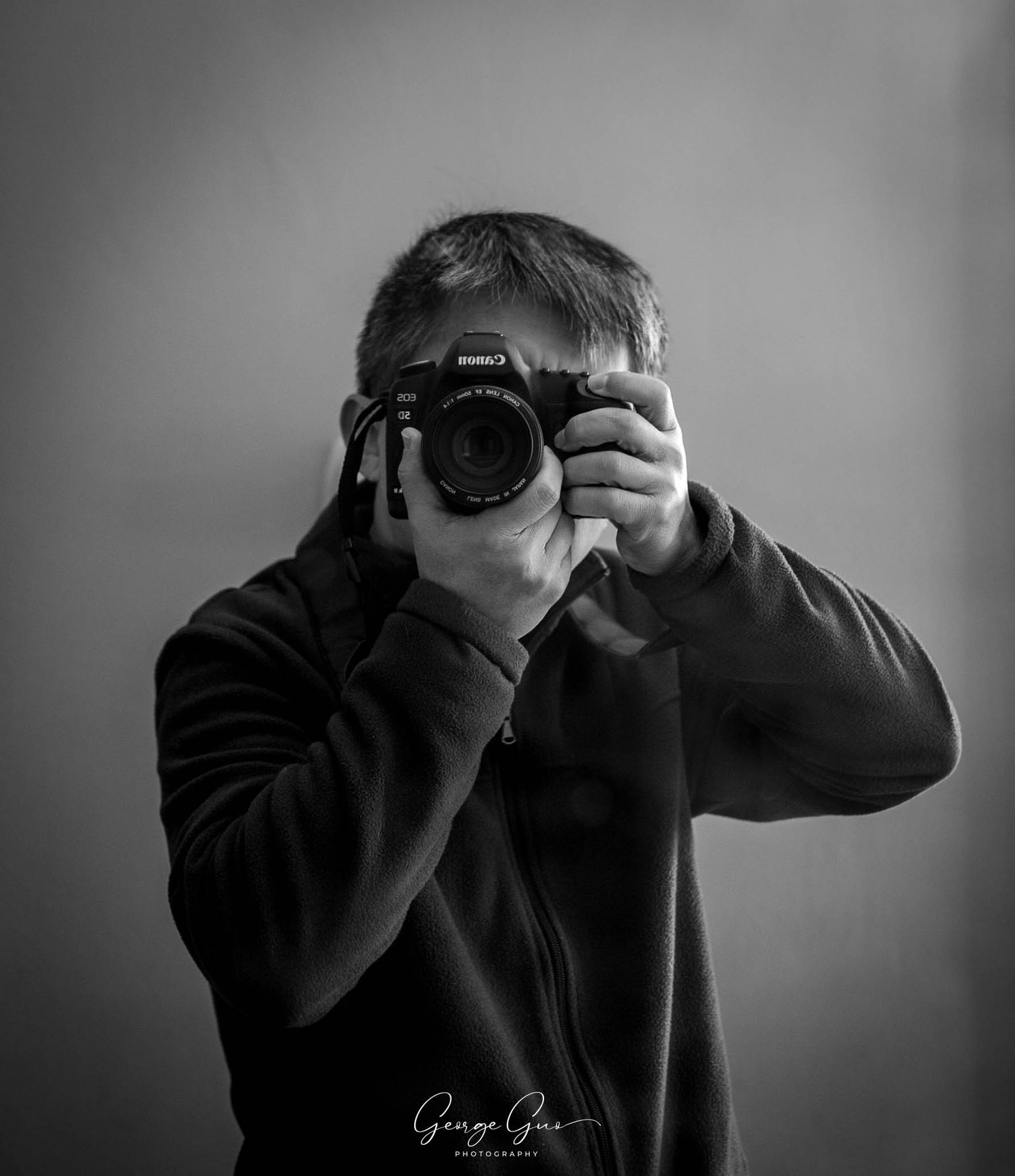 Self-portrait of George Guo Photographer holding a camera, captured in black and white by George Guo Photographer