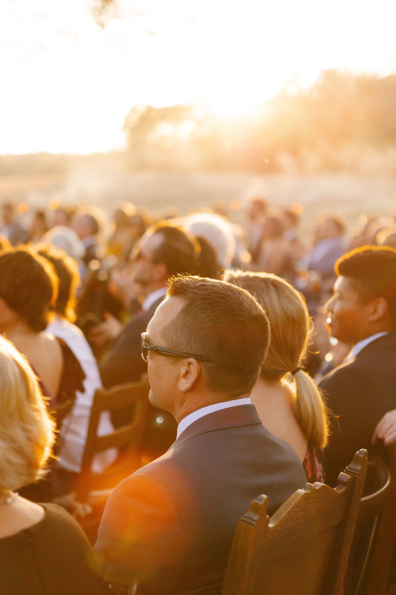 Silhouetted crowd of wedding guests backlit by golden sunset light.
