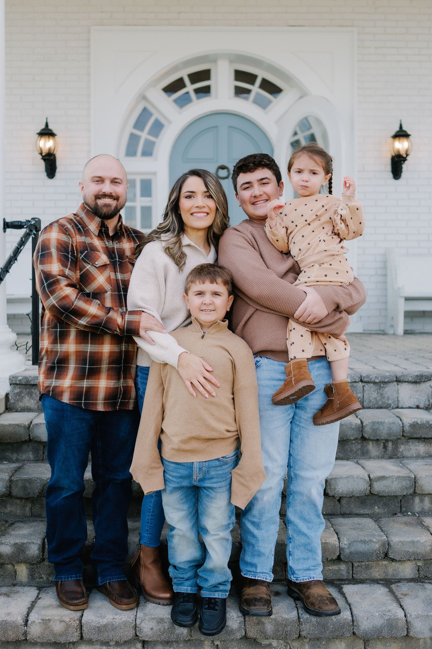 Family poses together on stone steps in front of white building with casual fall outfits.