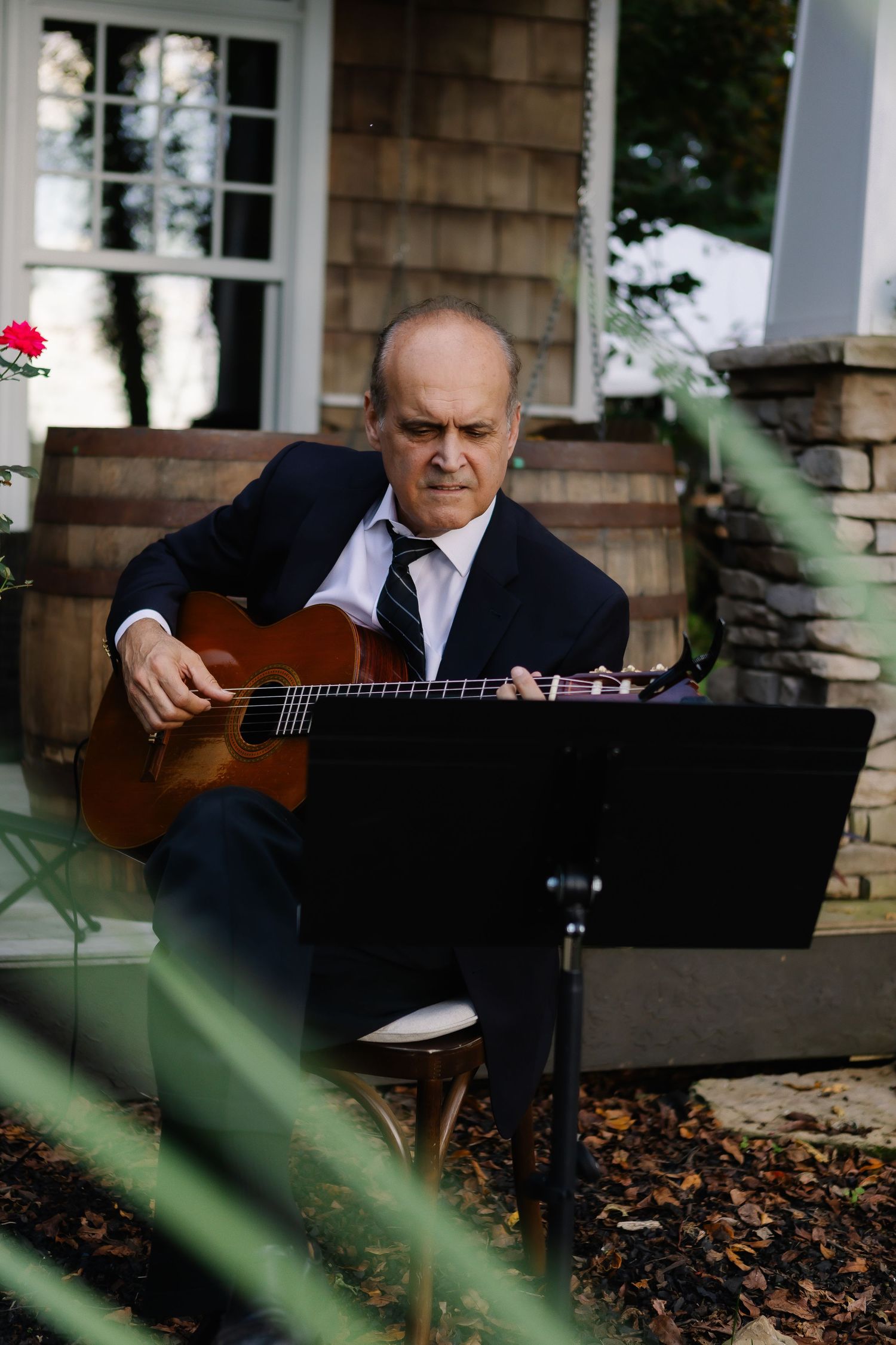 Musician playing acoustic guitar outdoors near a stone building.