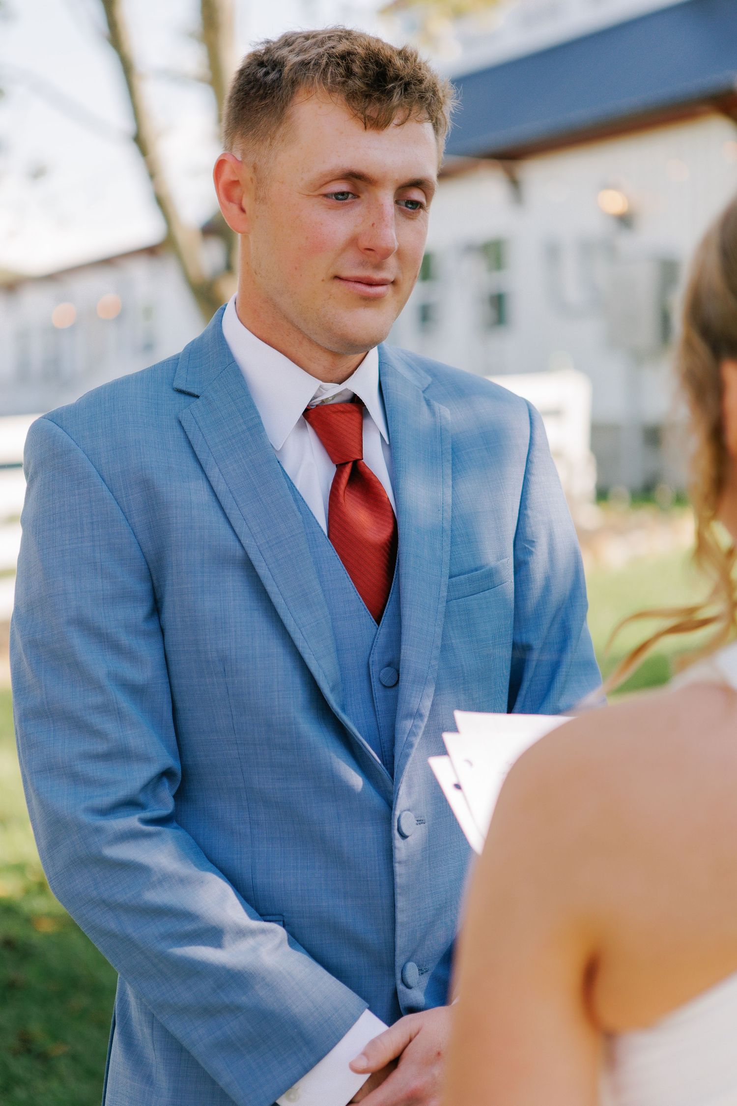 Wedding ceremony moment outdoors with blue suit and red tie.