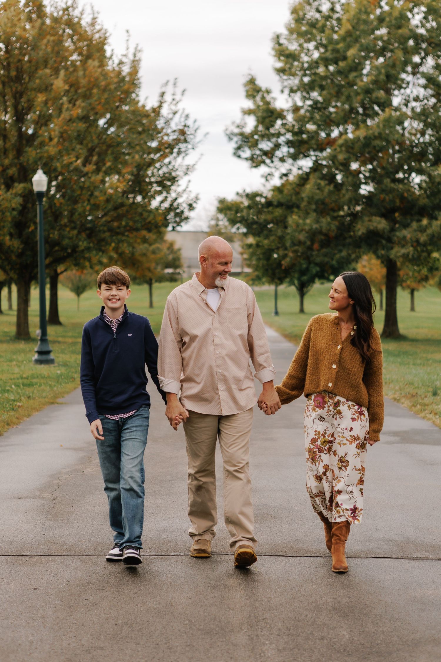 Three people walking together on tree-lined path during fall season.