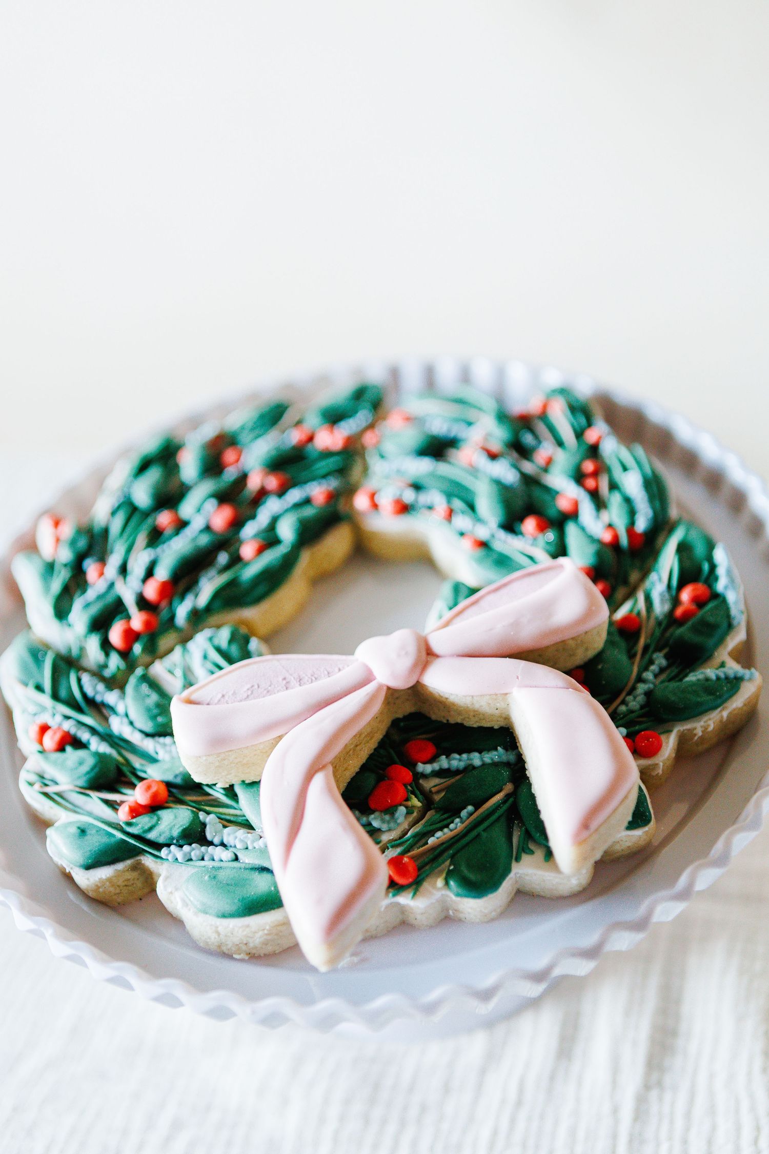 Christmas wreath sugar cookies decorated with green frosting and pink bows on a white plate.