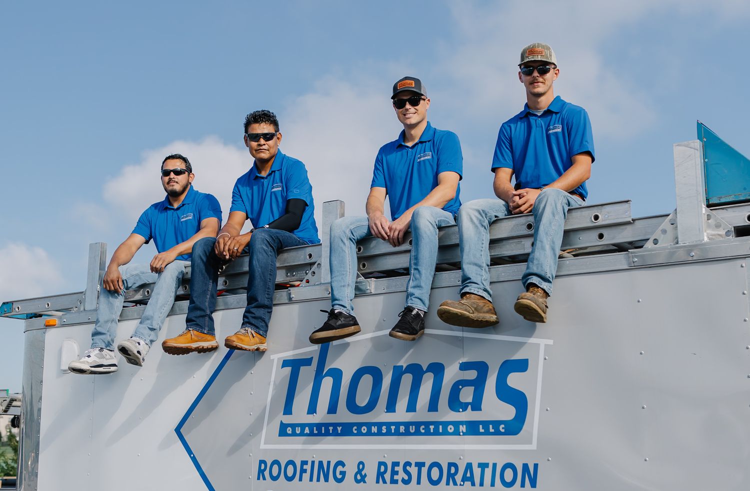 Team members in matching blue shirts seated on roofing equipment outdoors.