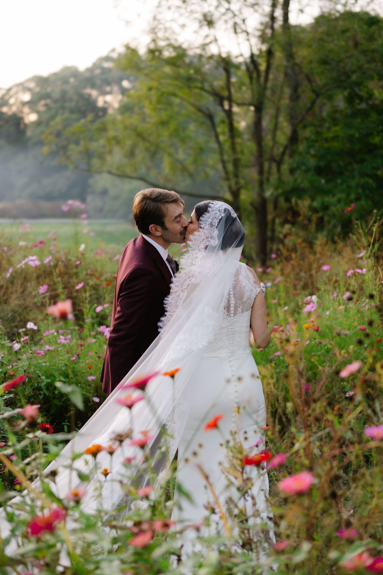 Wedding couple embracing in a wildflower meadow with pink flowers and flowing white dress.