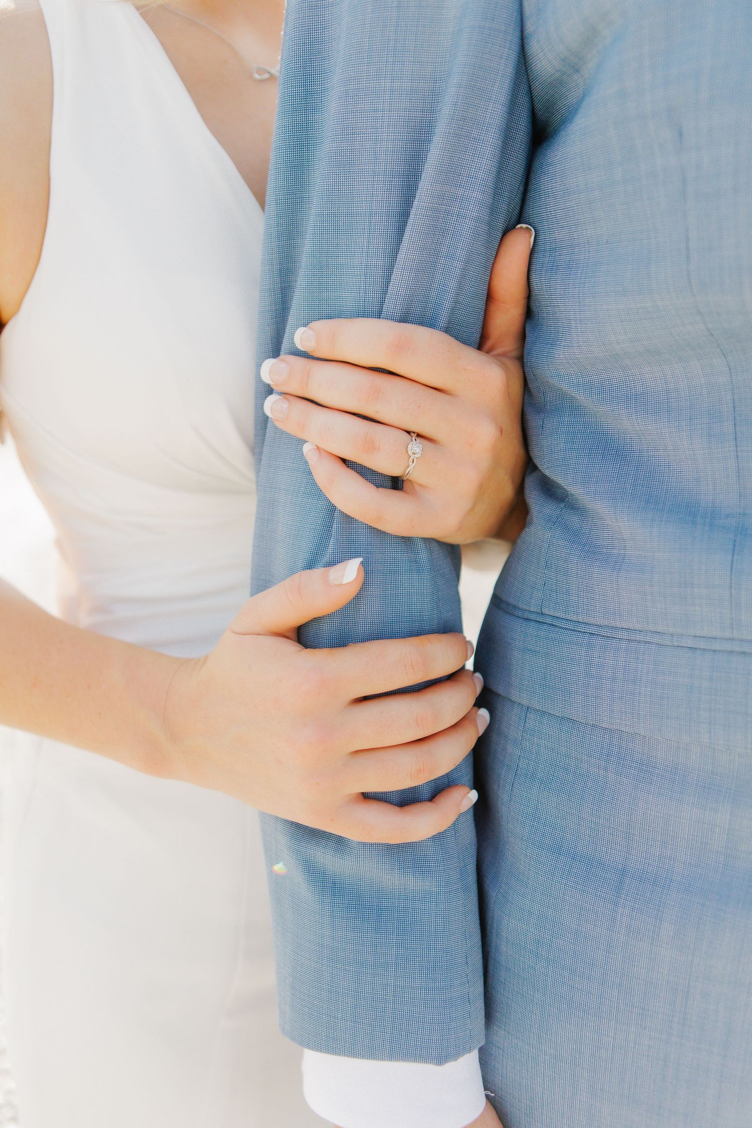 Close-up details of couple embracing showing light blue suit and white dress.