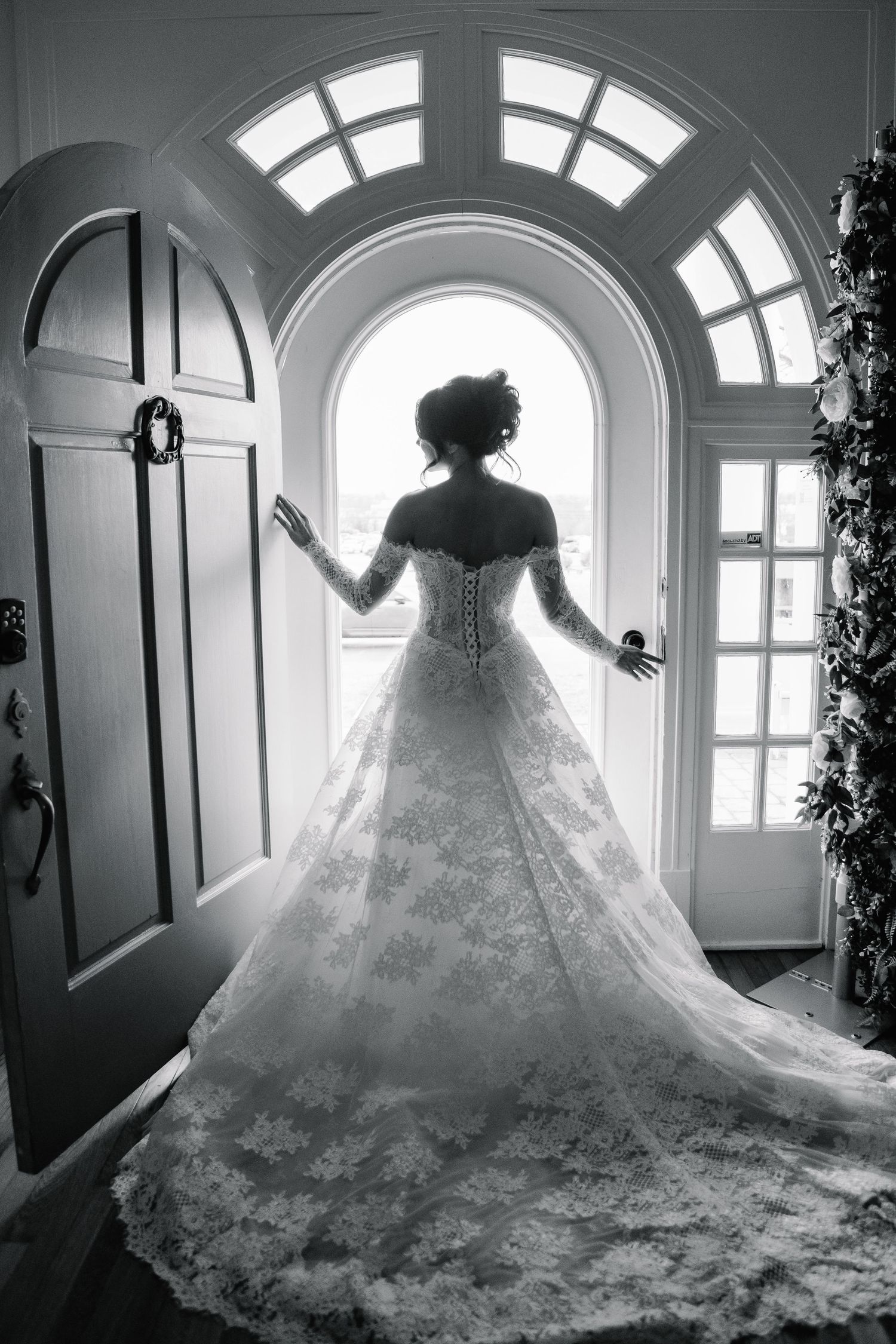 Black and white silhouette of bride in lace ball gown standing before arched doorway with dramatic train.