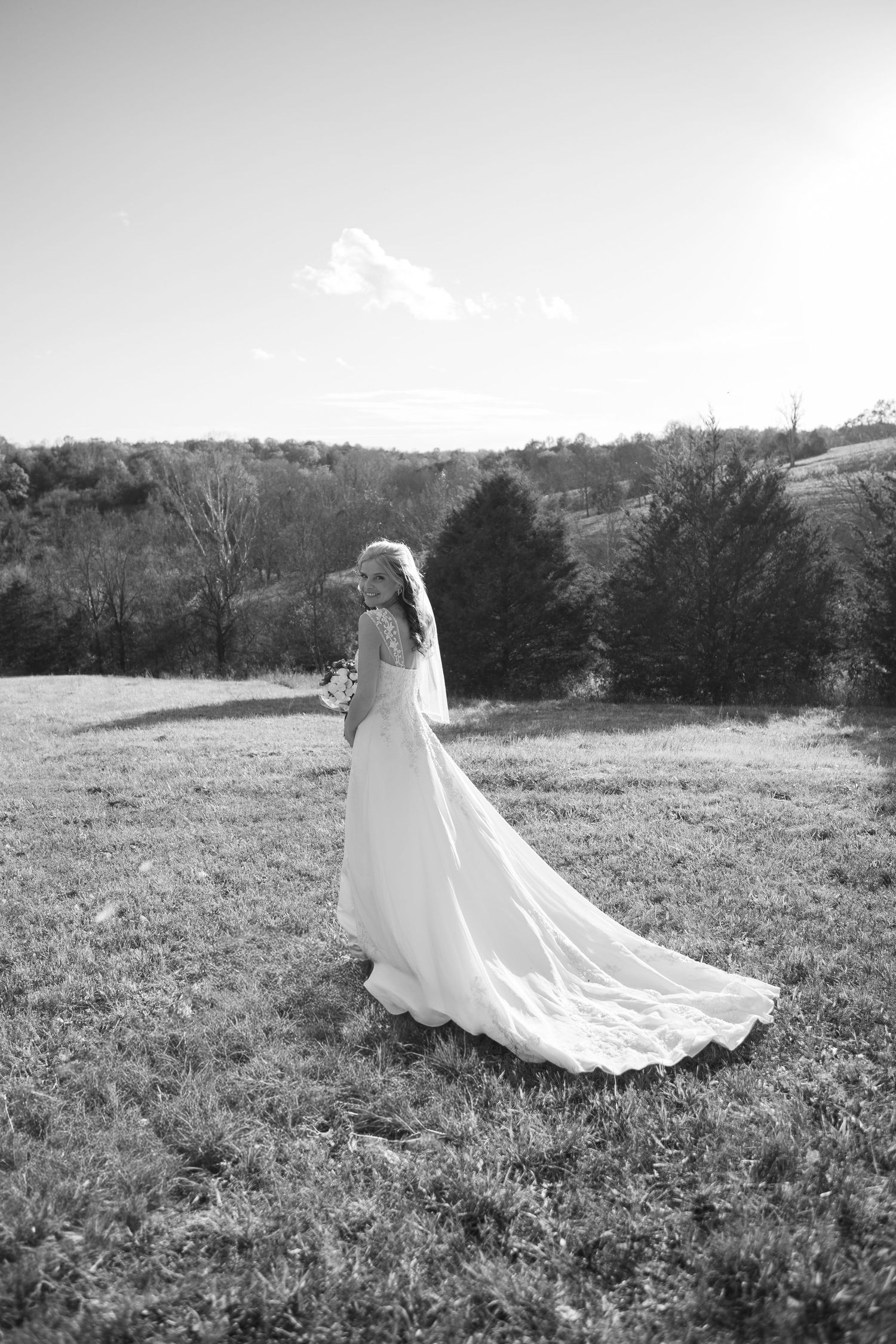 A flowing white wedding dress and veil captured in motion across a grassy field.