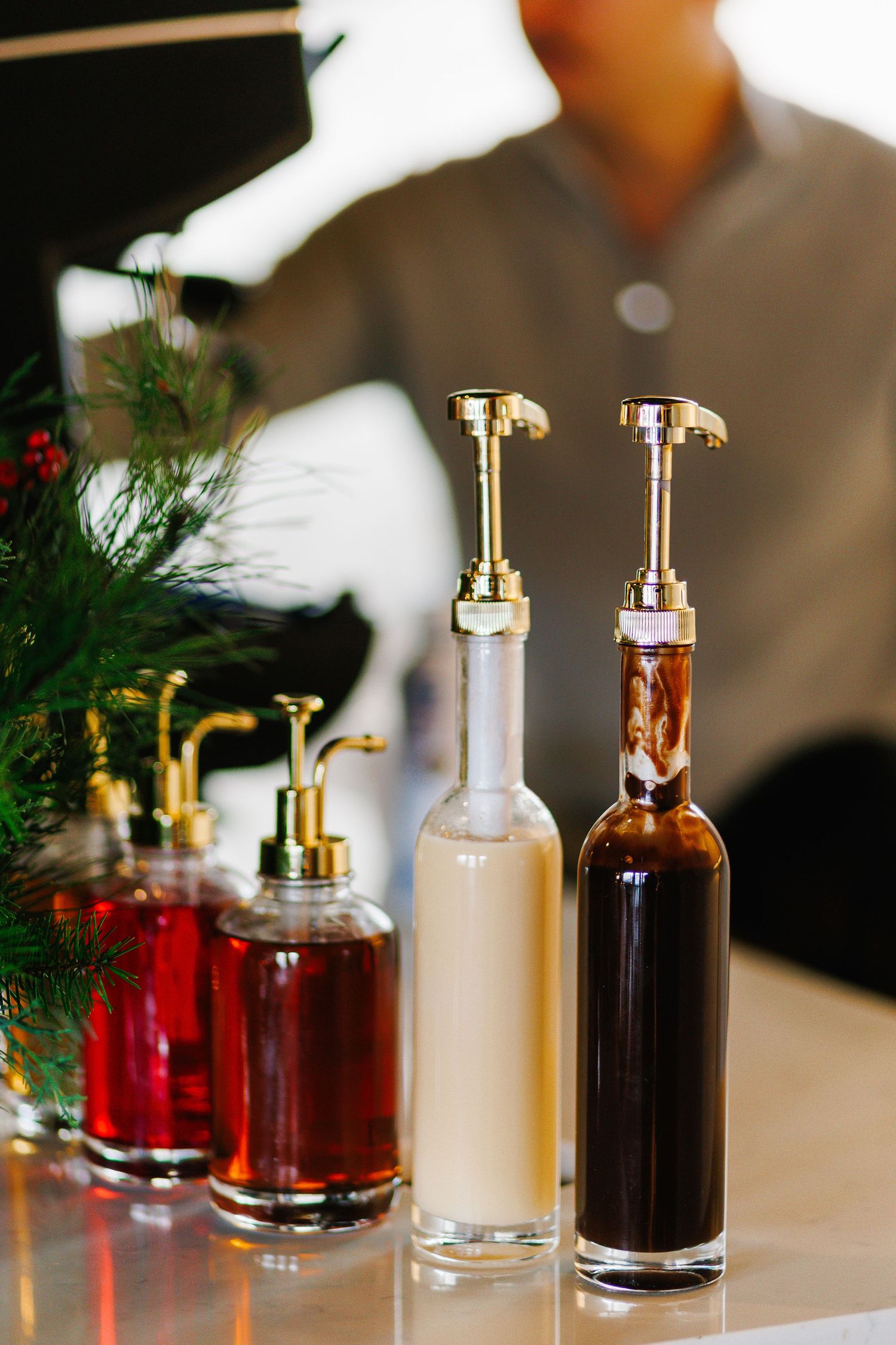 Row of elegant glass bottles with gold pumps containing holiday cocktail ingredients.