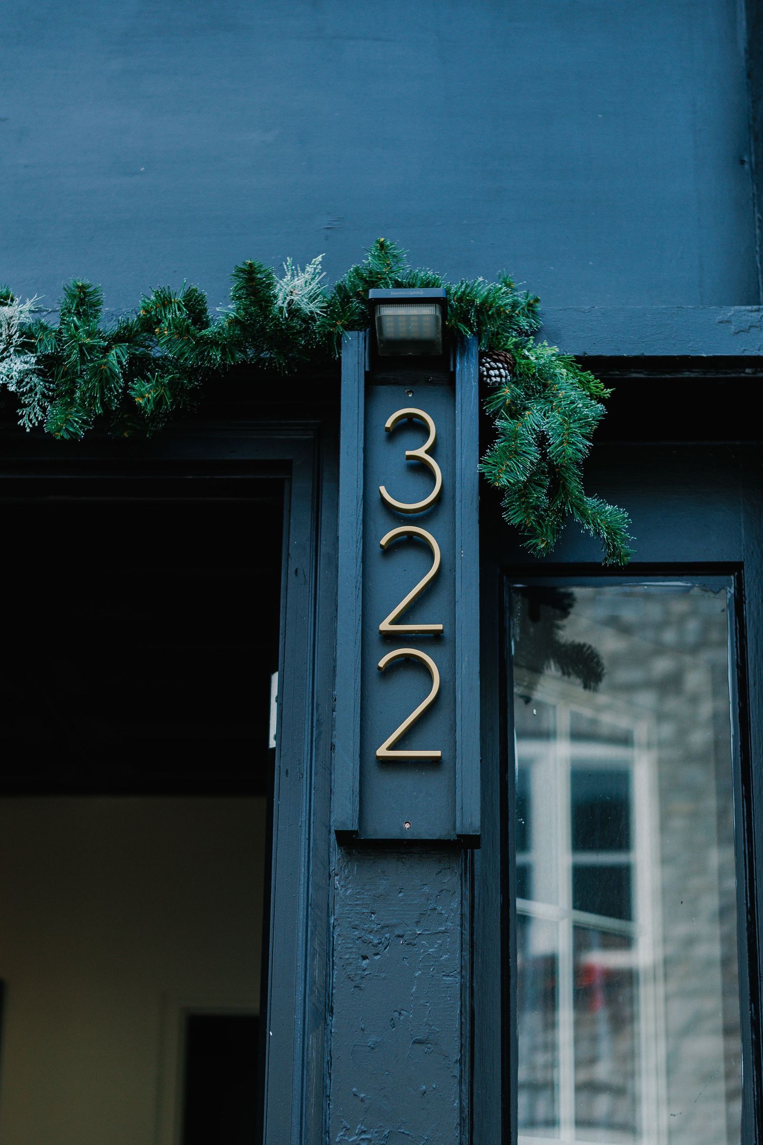 Modern house numbers in metallic finish mounted on dark blue exterior wall.