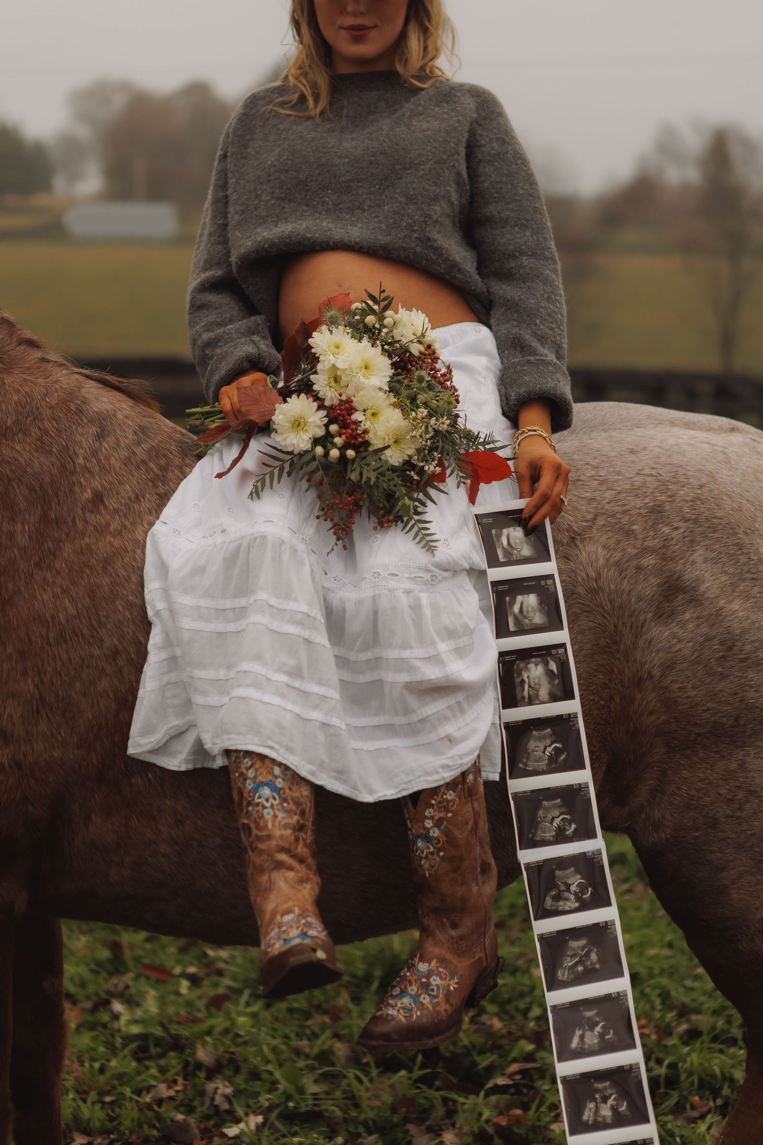 Pregnancy announcement with ultrasound photos and flowers against rustic farm backdrop.