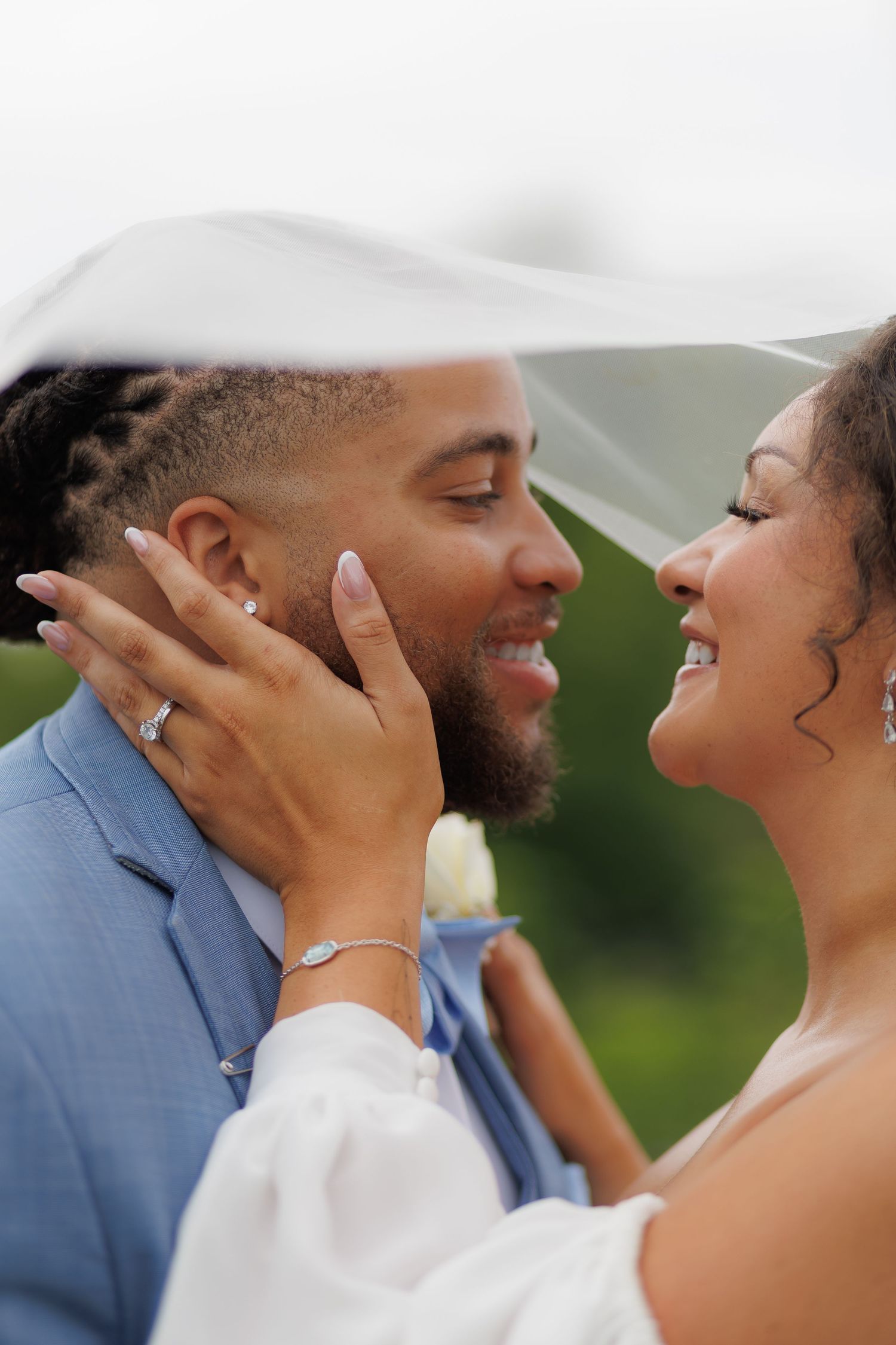 A joyful bride and groom share an intimate moment under a veil, smiling at each other on their wedding day.