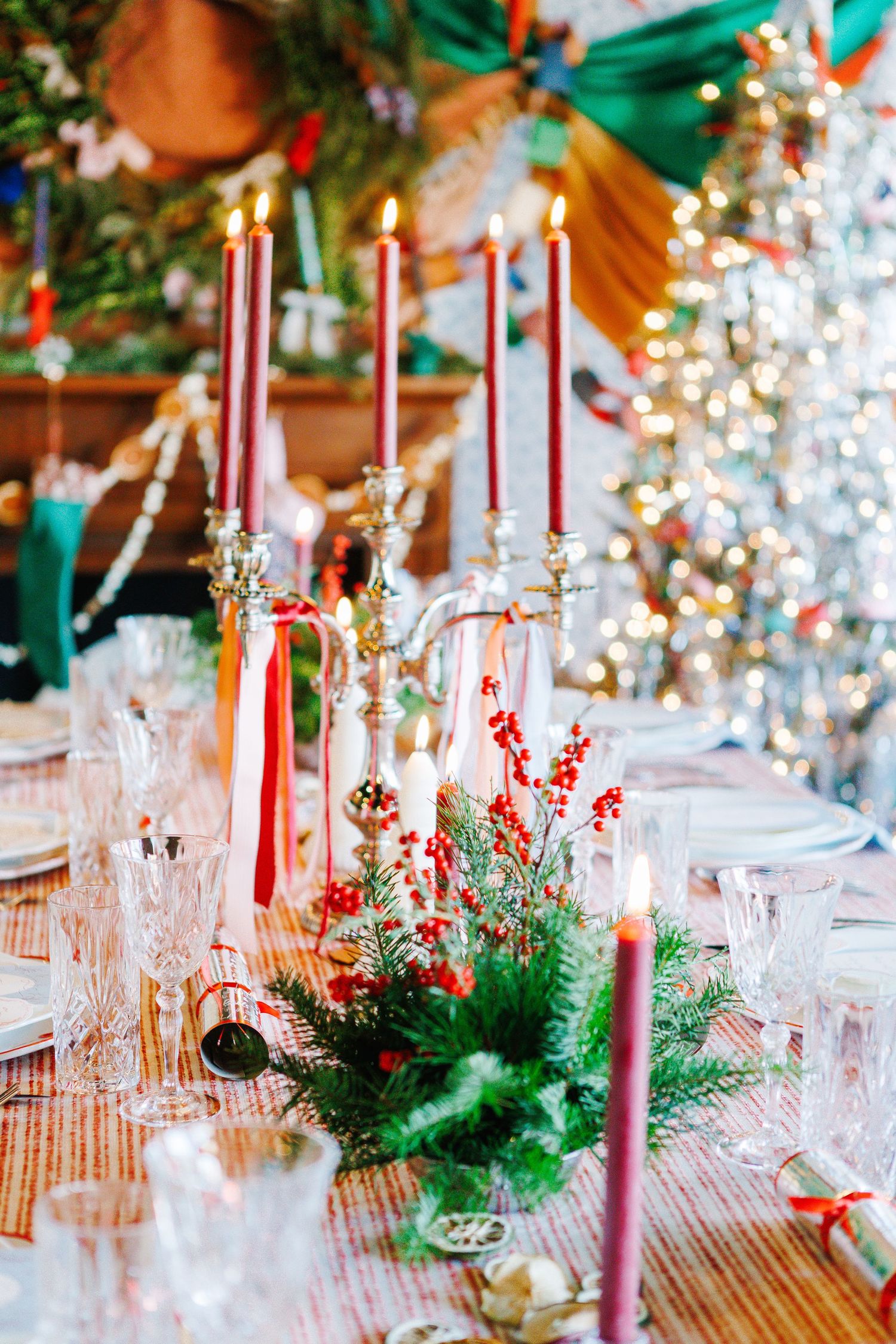 Elegant holiday table setting with red candles, pine greenery, and sparkling Christmas decorations.