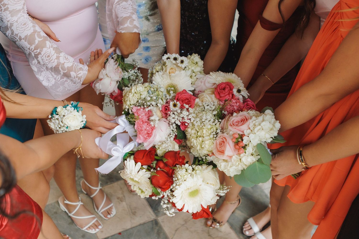 A group gathers around a beautiful wedding bouquet featuring red and white flowers with baby's breath accents.